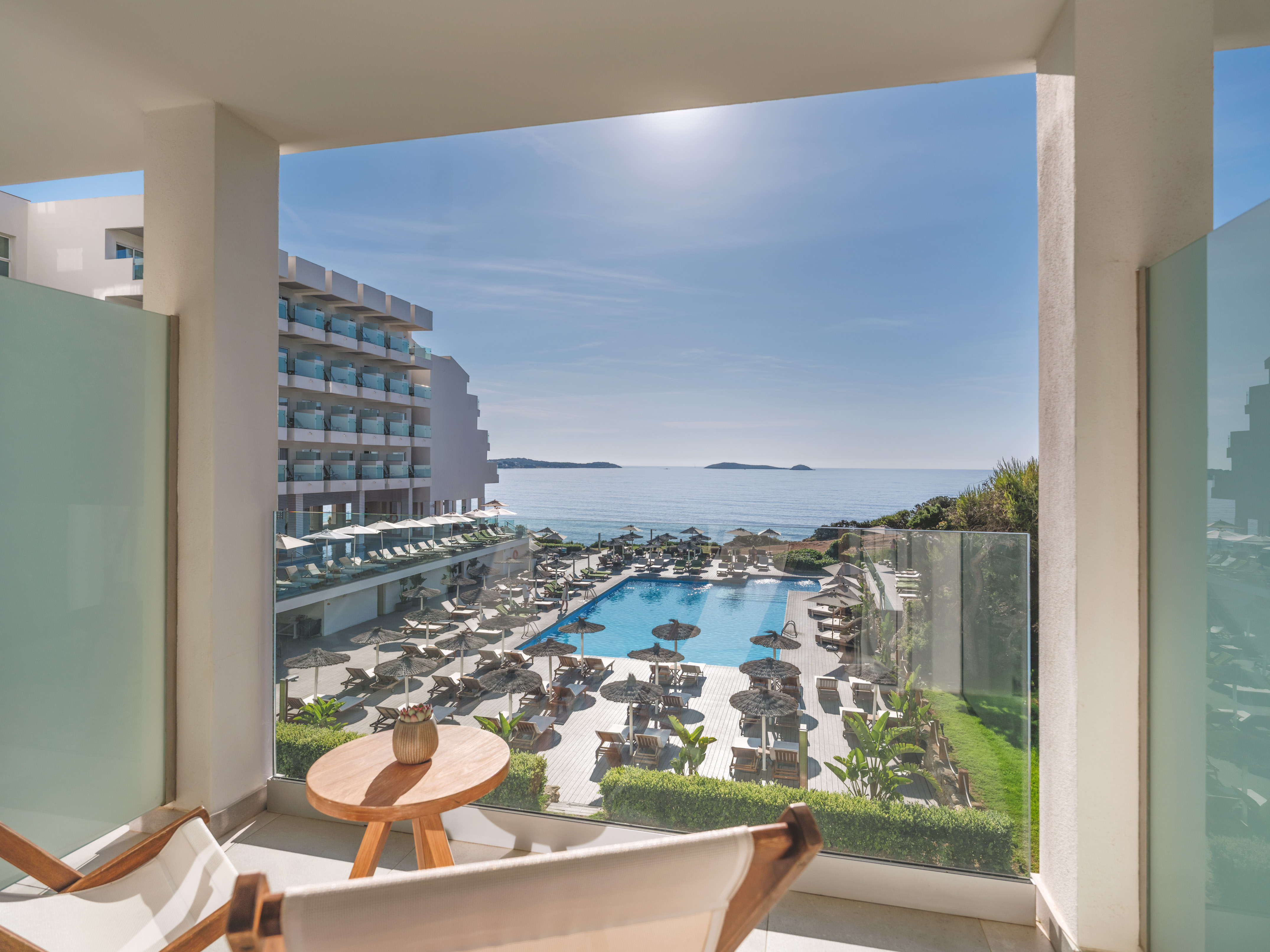 Sunny hotel balcony view of ocean, large swimming pool, and resort grounds.