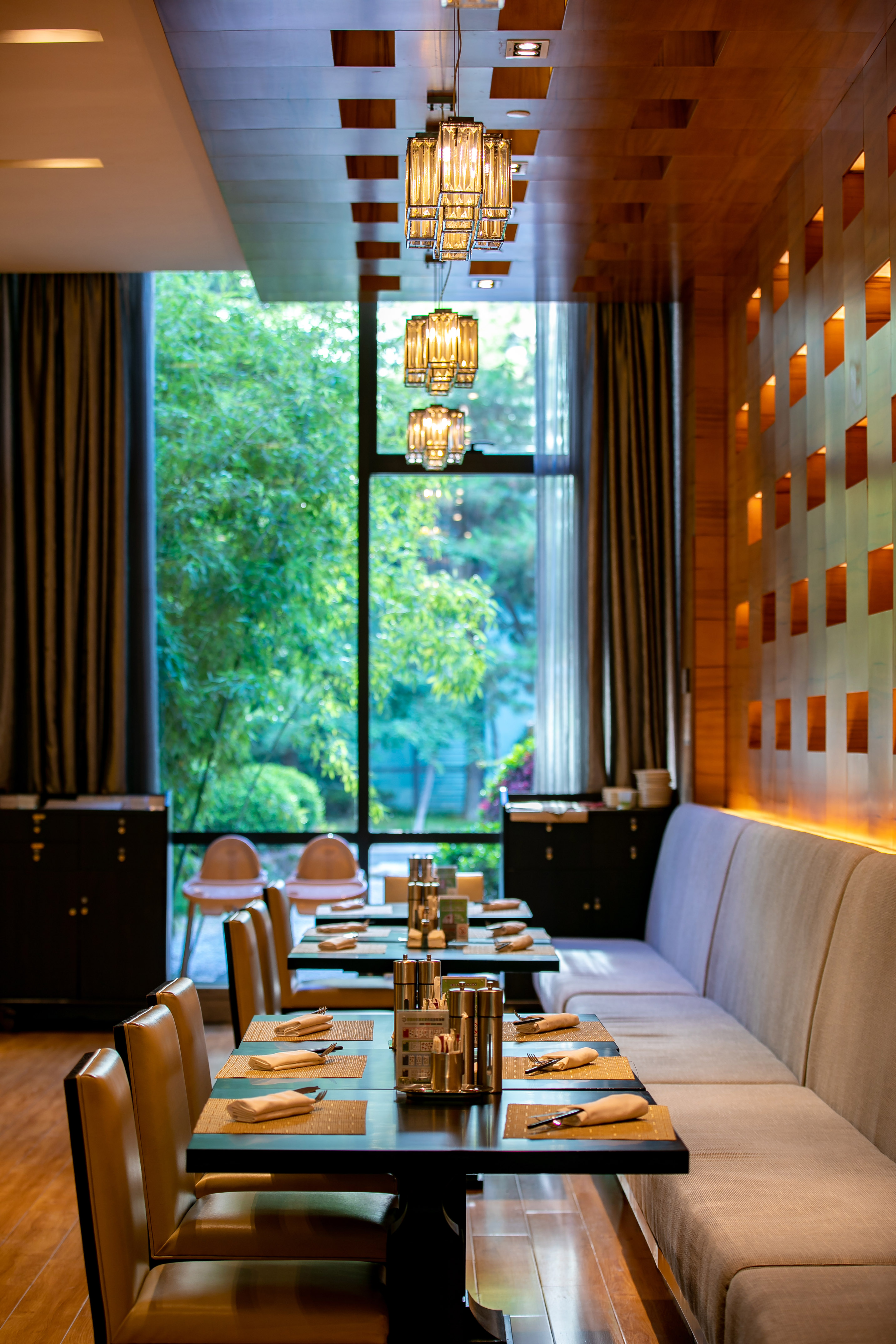 Modern restaurant interior, set dining tables, elegant chandeliers, garden view.
