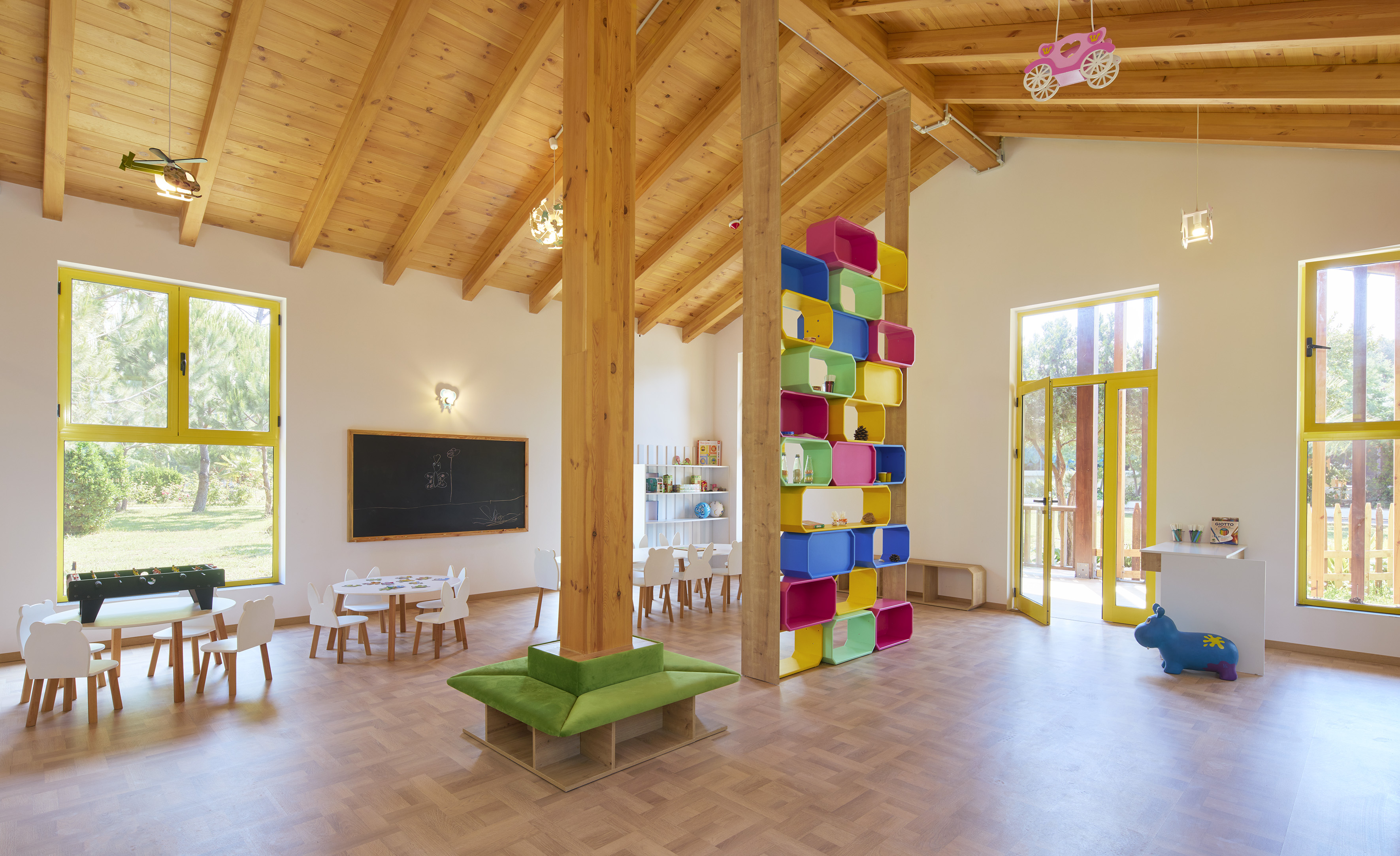Bright children's playroom with colorful storage cubbies, wooden ceiling, and small tables.