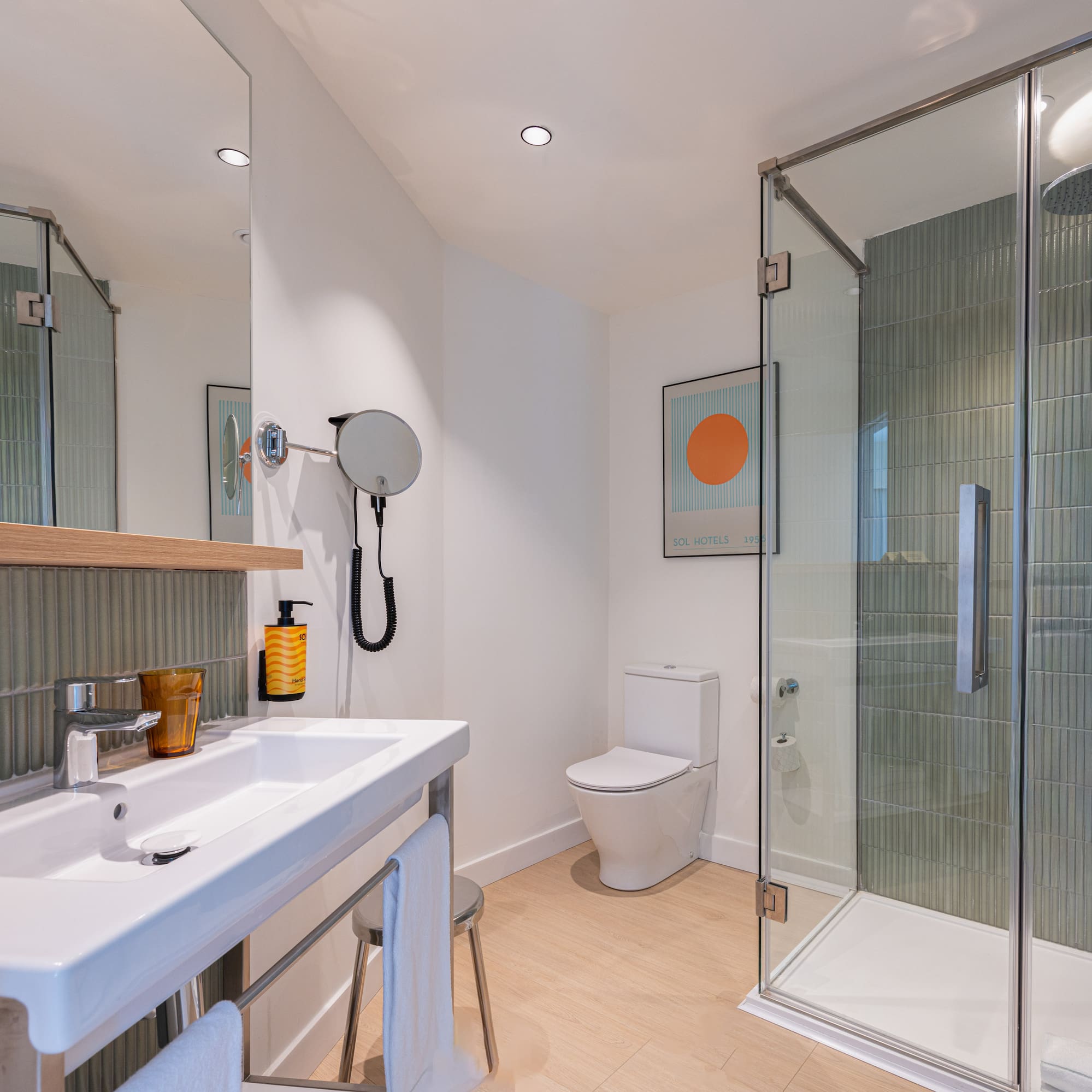 Contemporary hotel bathroom: glass shower, white sink, toilet, and green tiled walls.
