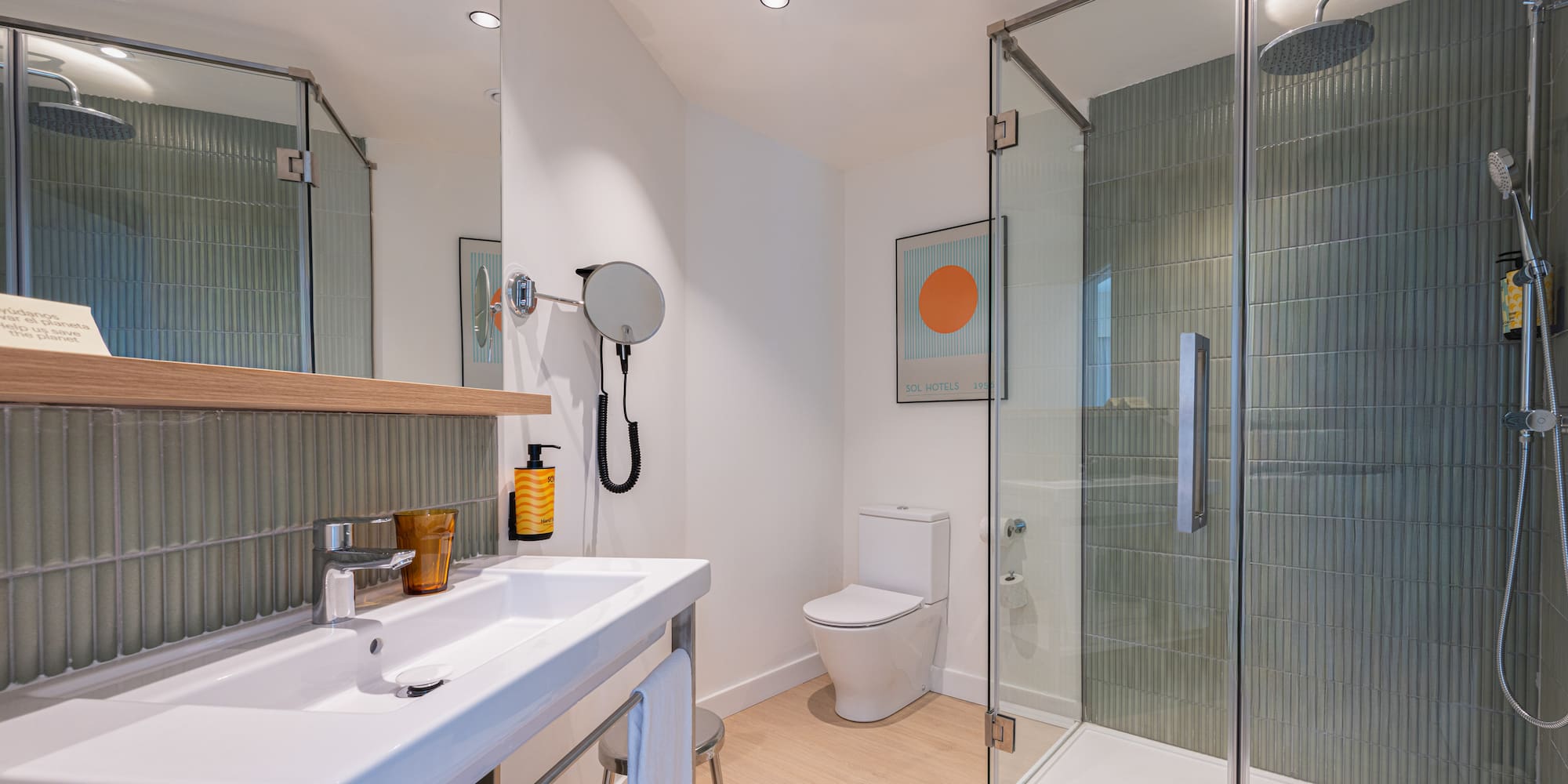 Contemporary hotel bathroom: glass shower, white sink, toilet, and green tiled walls.