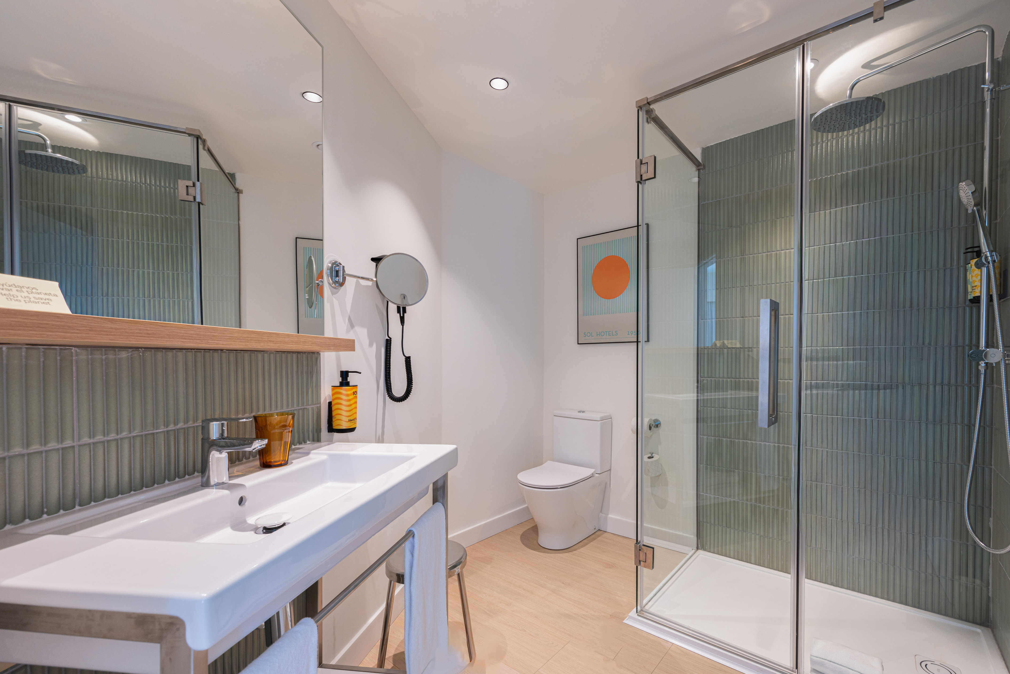 Modern hotel bathroom with walk-in shower, white sink, and green tiles.