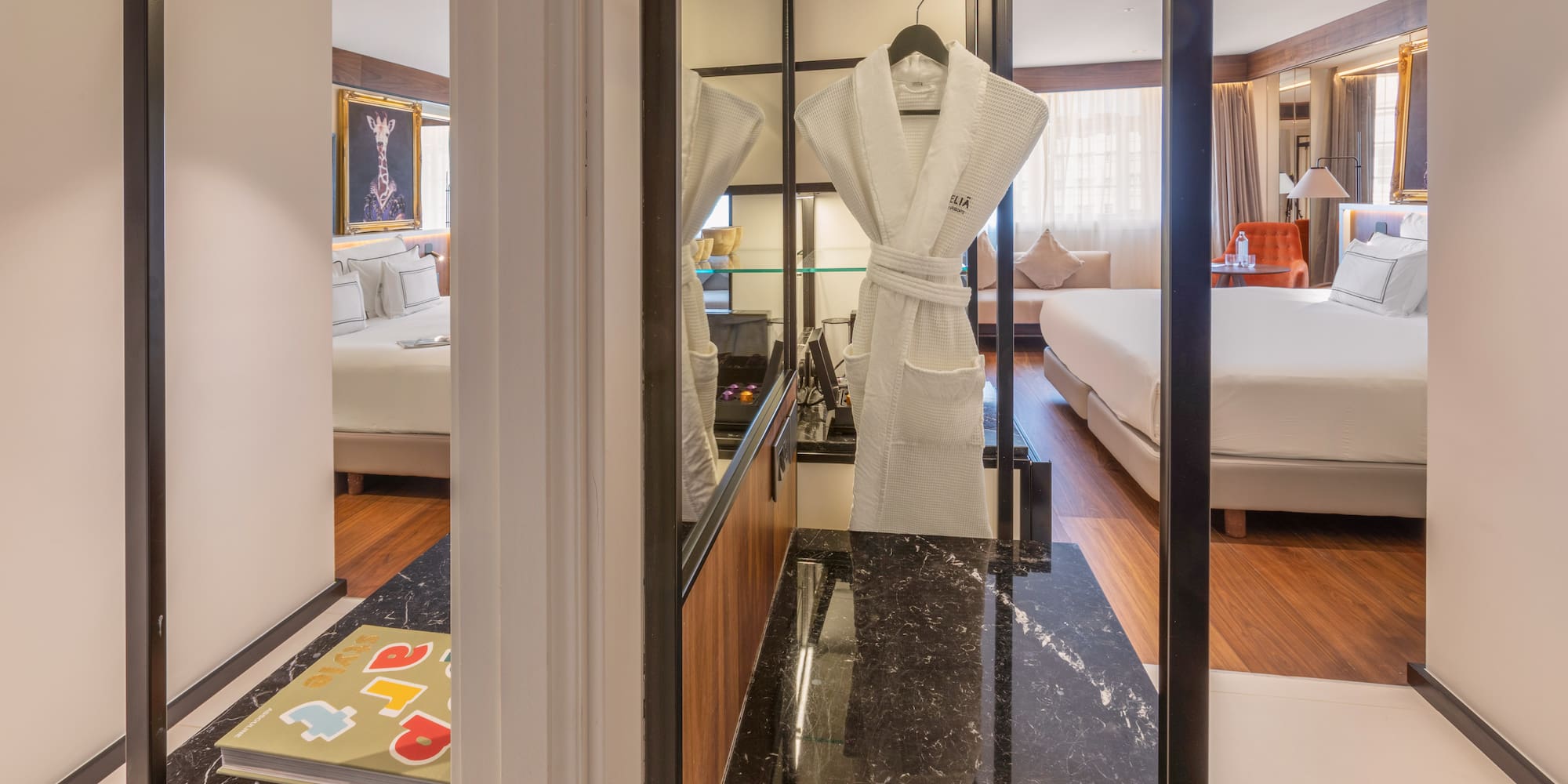 Modern hotel suite with bed, white bathrobe, and dark marble counter.