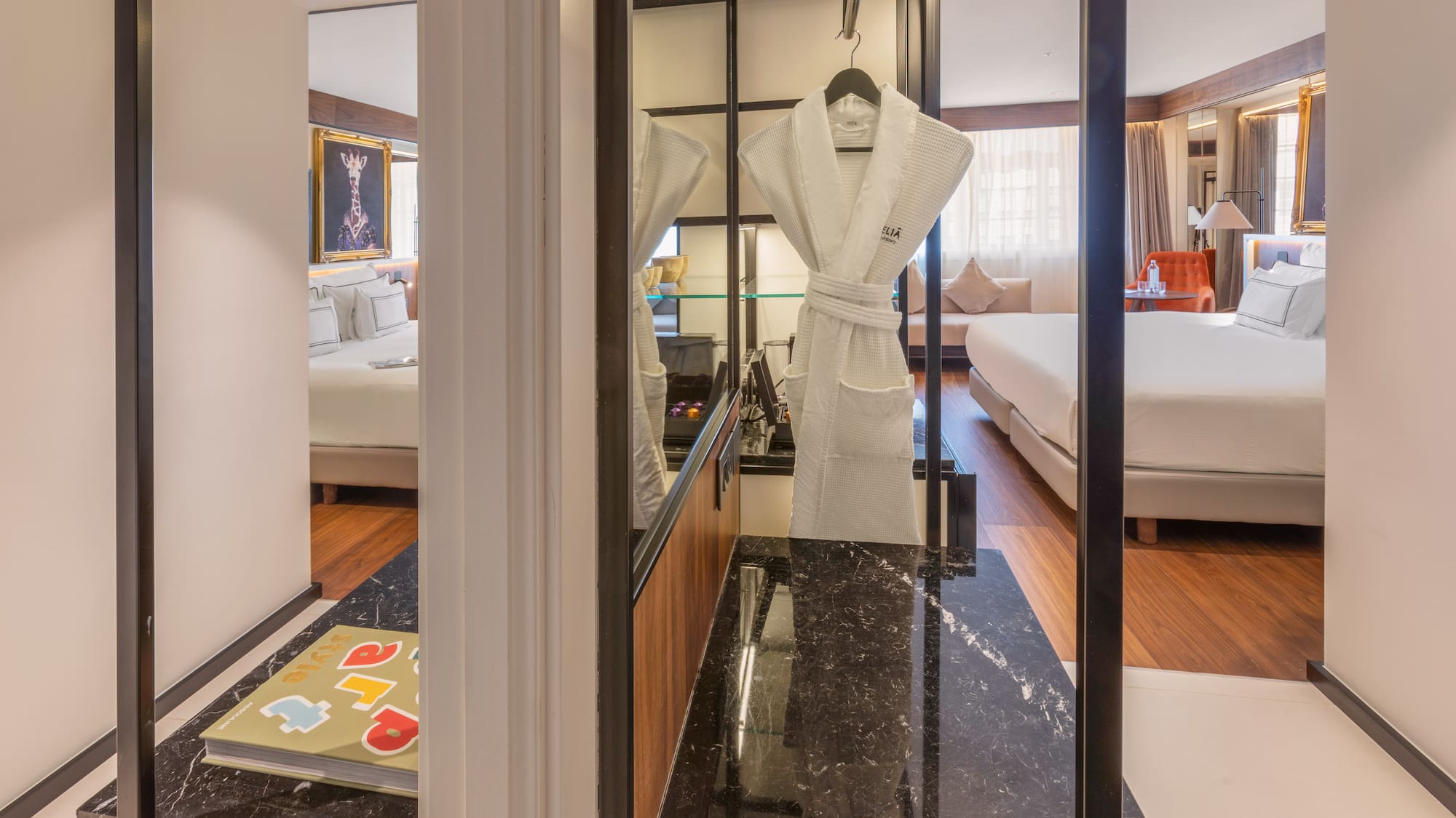 Modern hotel suite with bed, white bathrobe, and dark marble counter.