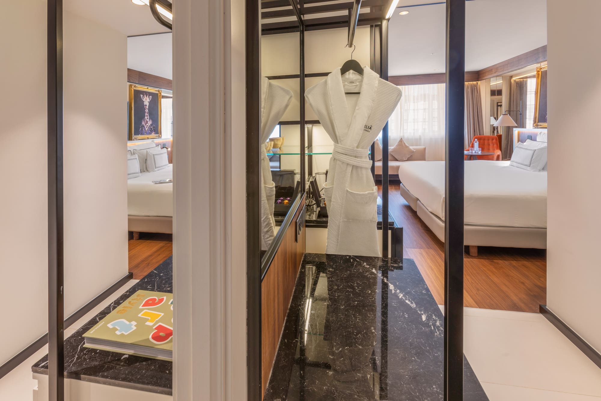 Modern hotel suite with bed, white bathrobe, and dark marble counter.