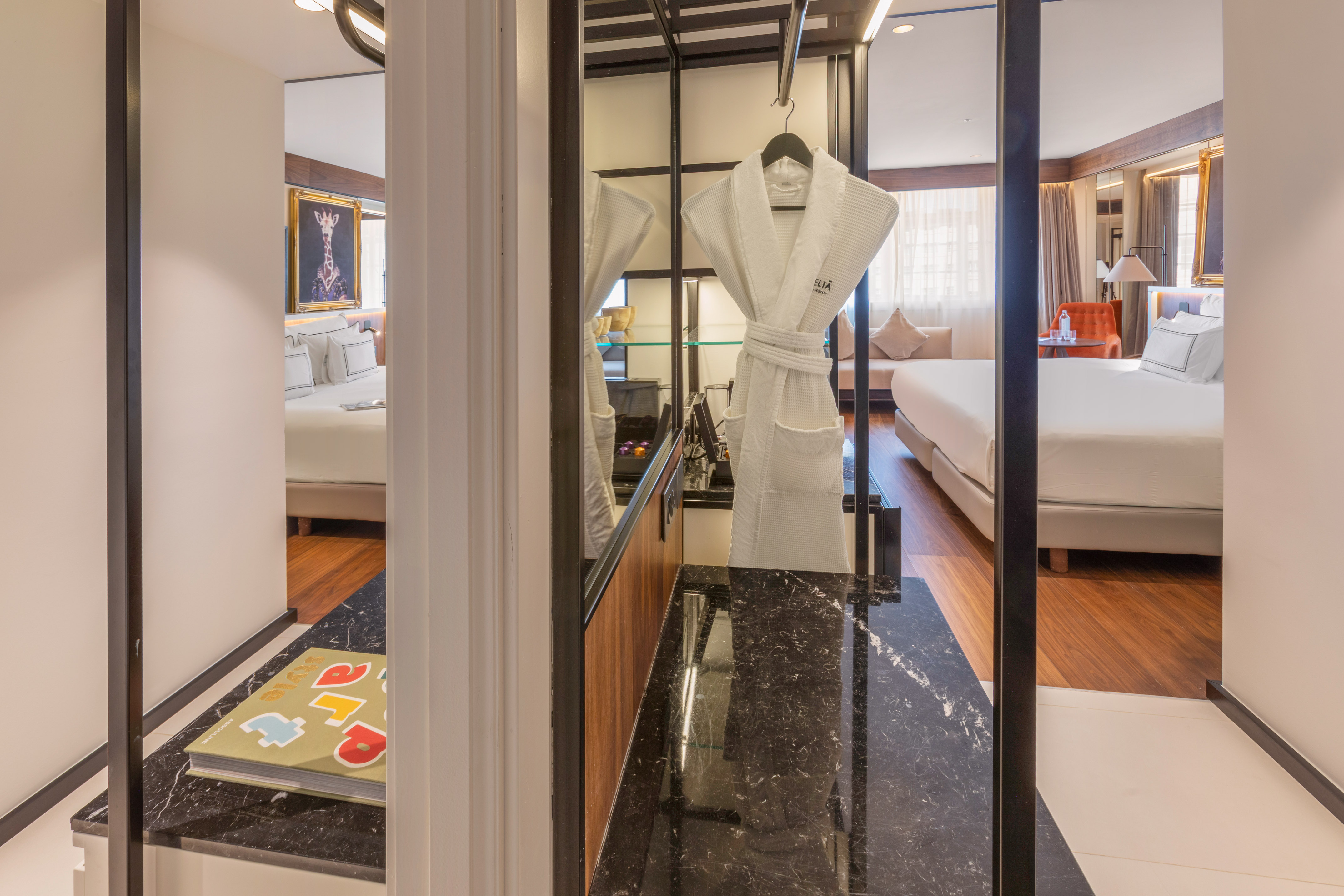 Modern hotel suite with bed, white bathrobe, and dark marble counter.