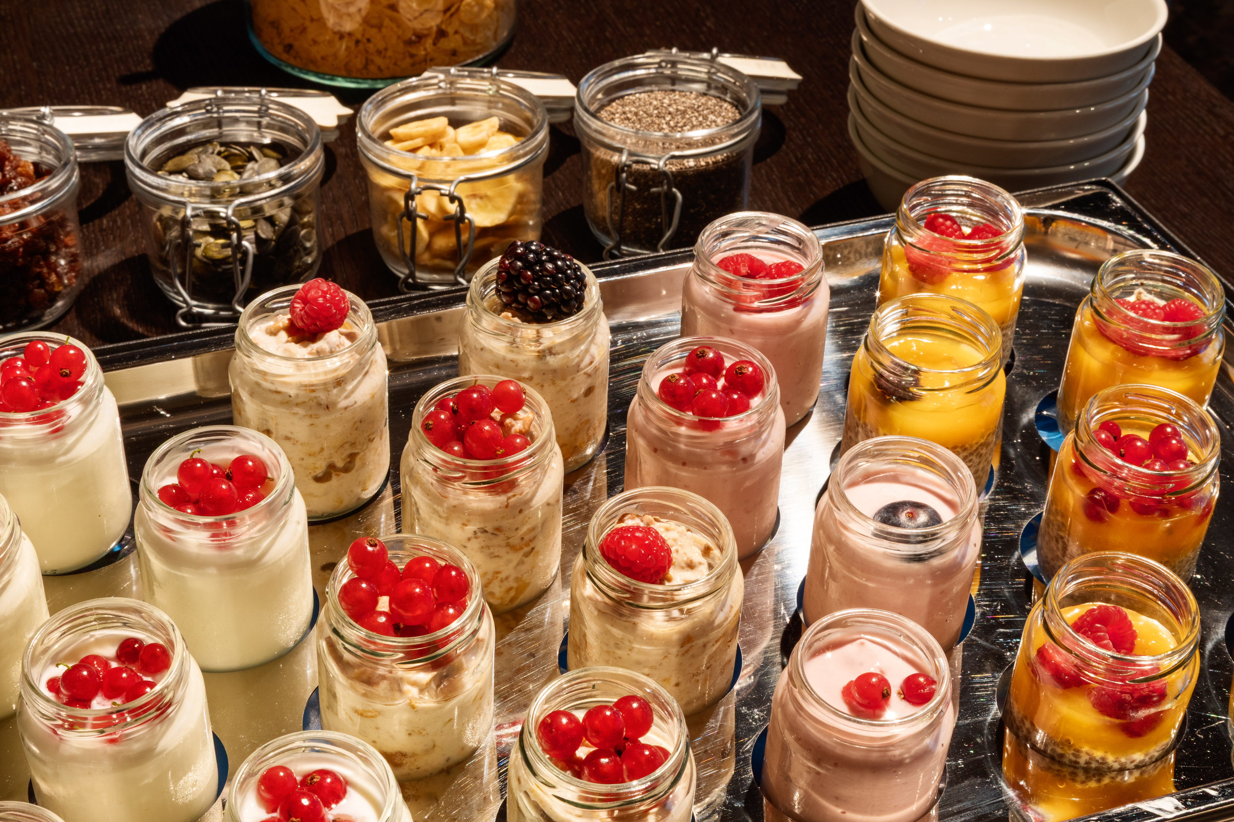 Assorted breakfast jars with yogurt, chia pudding, fresh berries, and seeds on a tray.