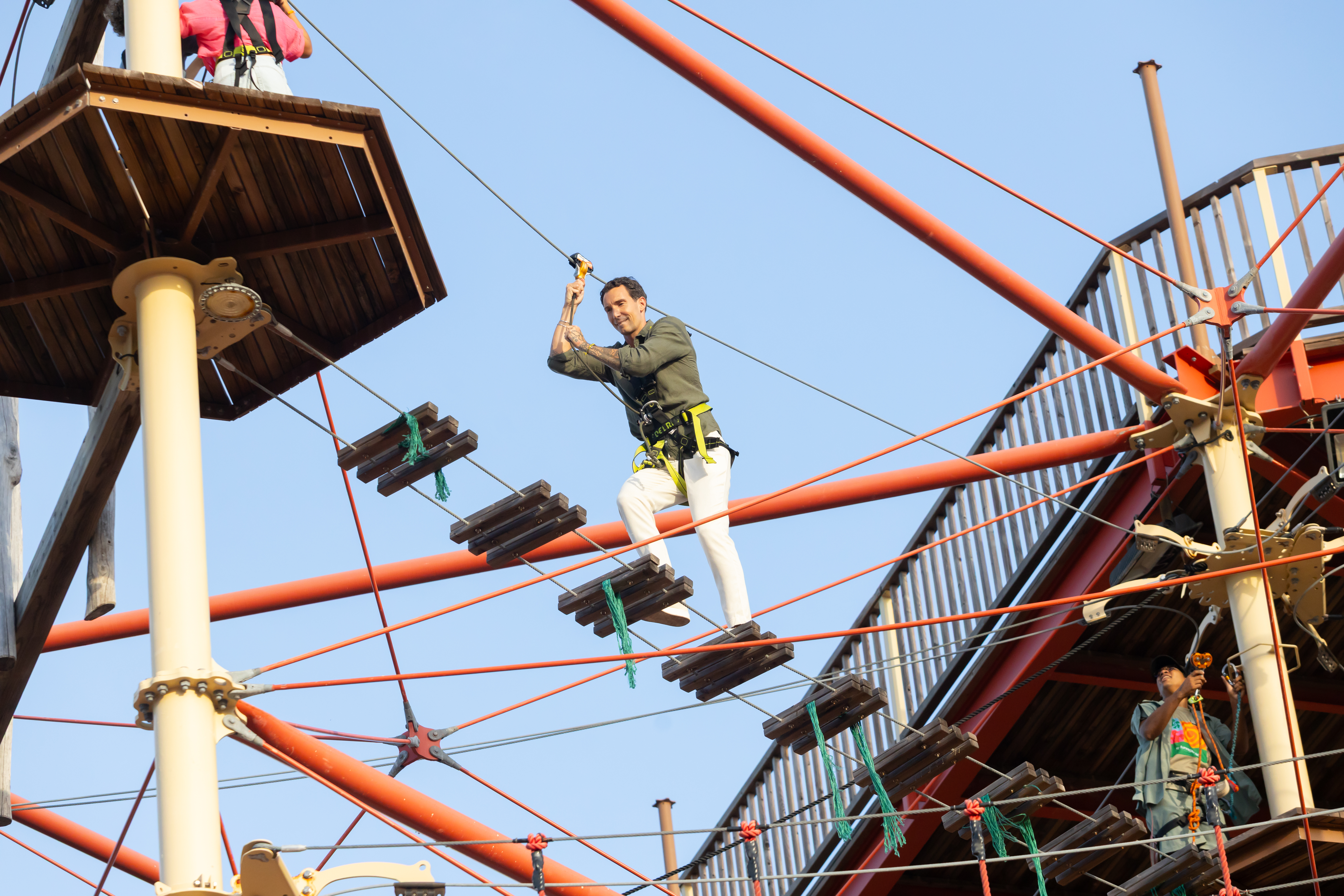 Man in harness navigating high ropes challenge course, balancing on wooden steps.