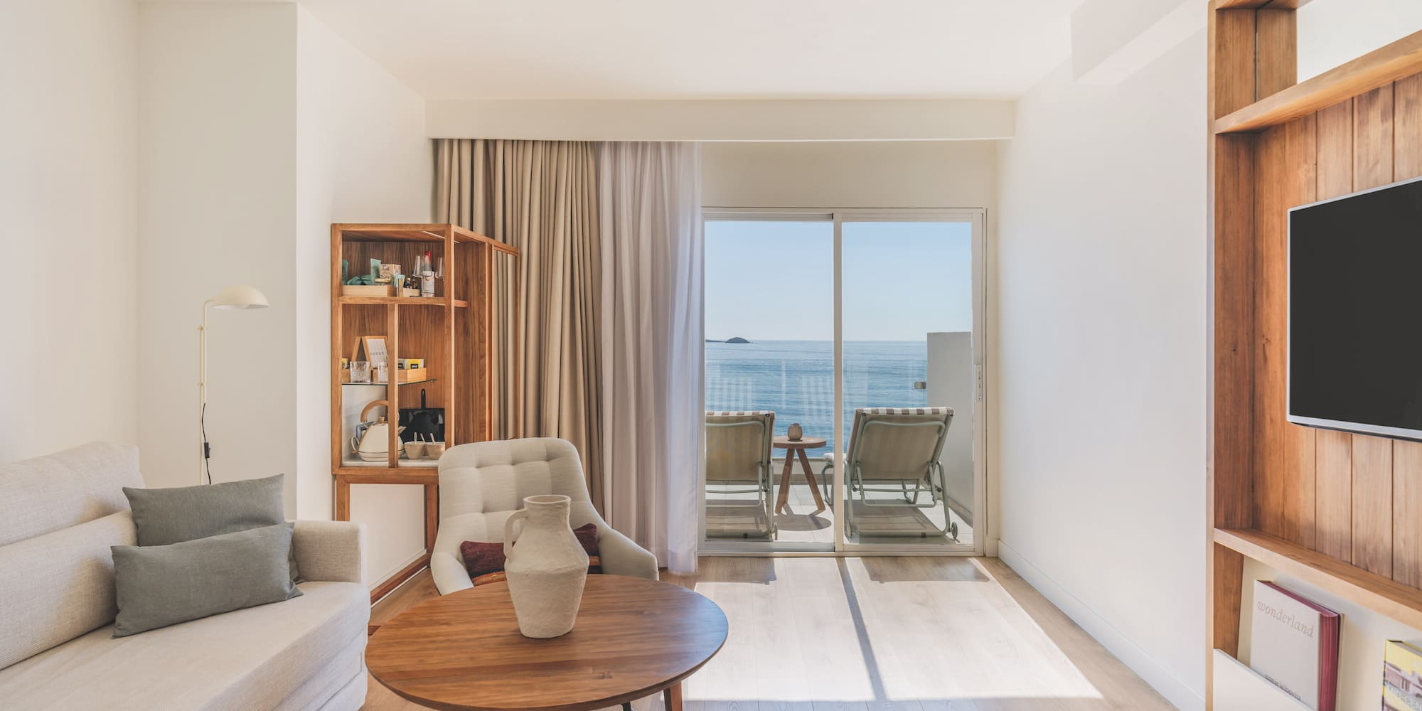 Modern hotel living room with ocean view balcony, light sofa, and wood accents.