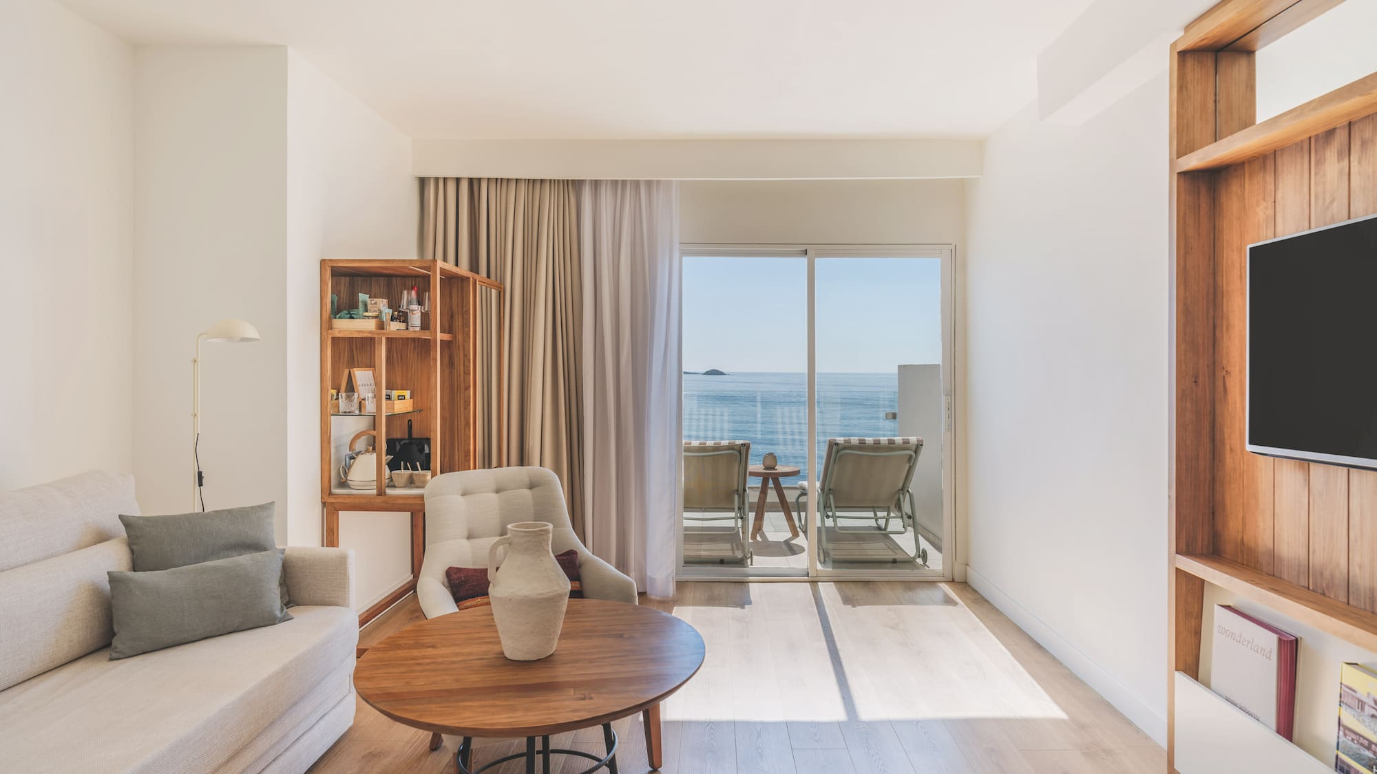 Modern hotel living room with ocean view balcony, light sofa, and wood accents.