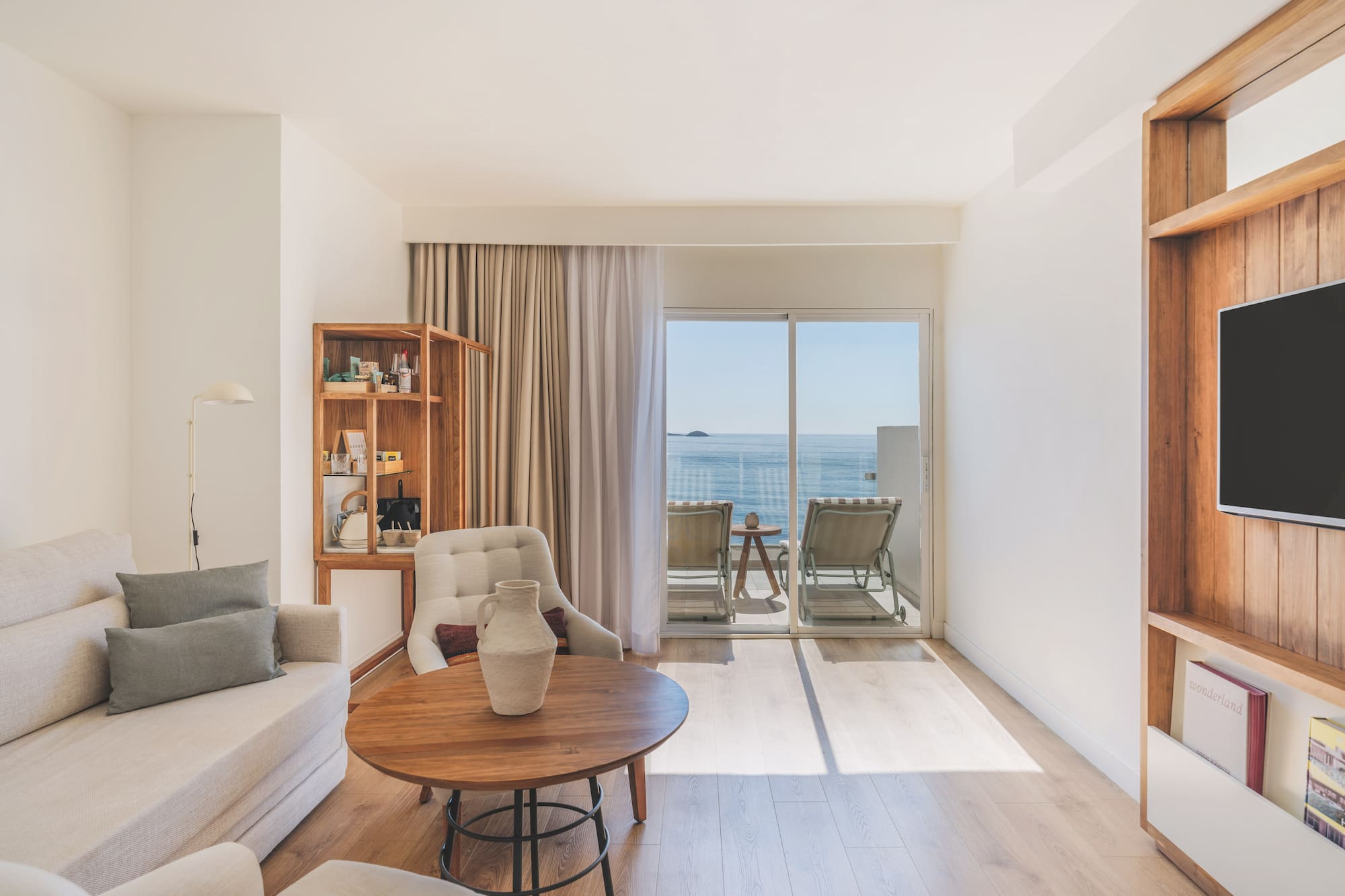 Modern hotel living room with ocean view balcony, light sofa, and wood accents.