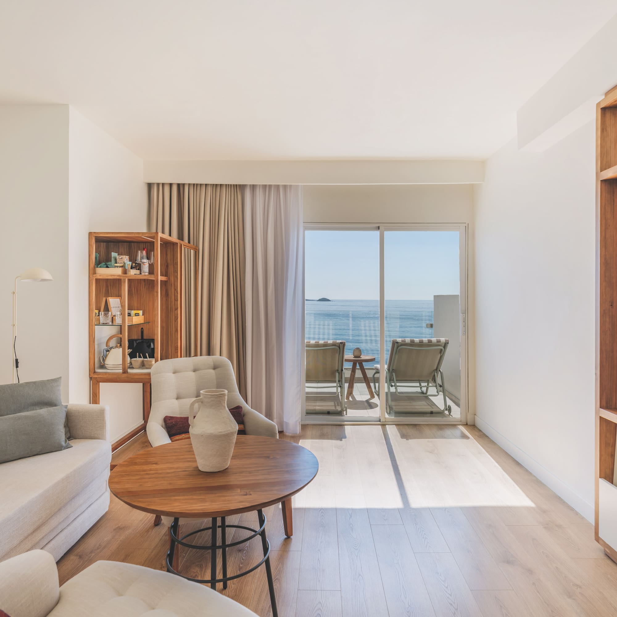 Modern hotel living room with ocean view balcony, light sofa, and wood accents.