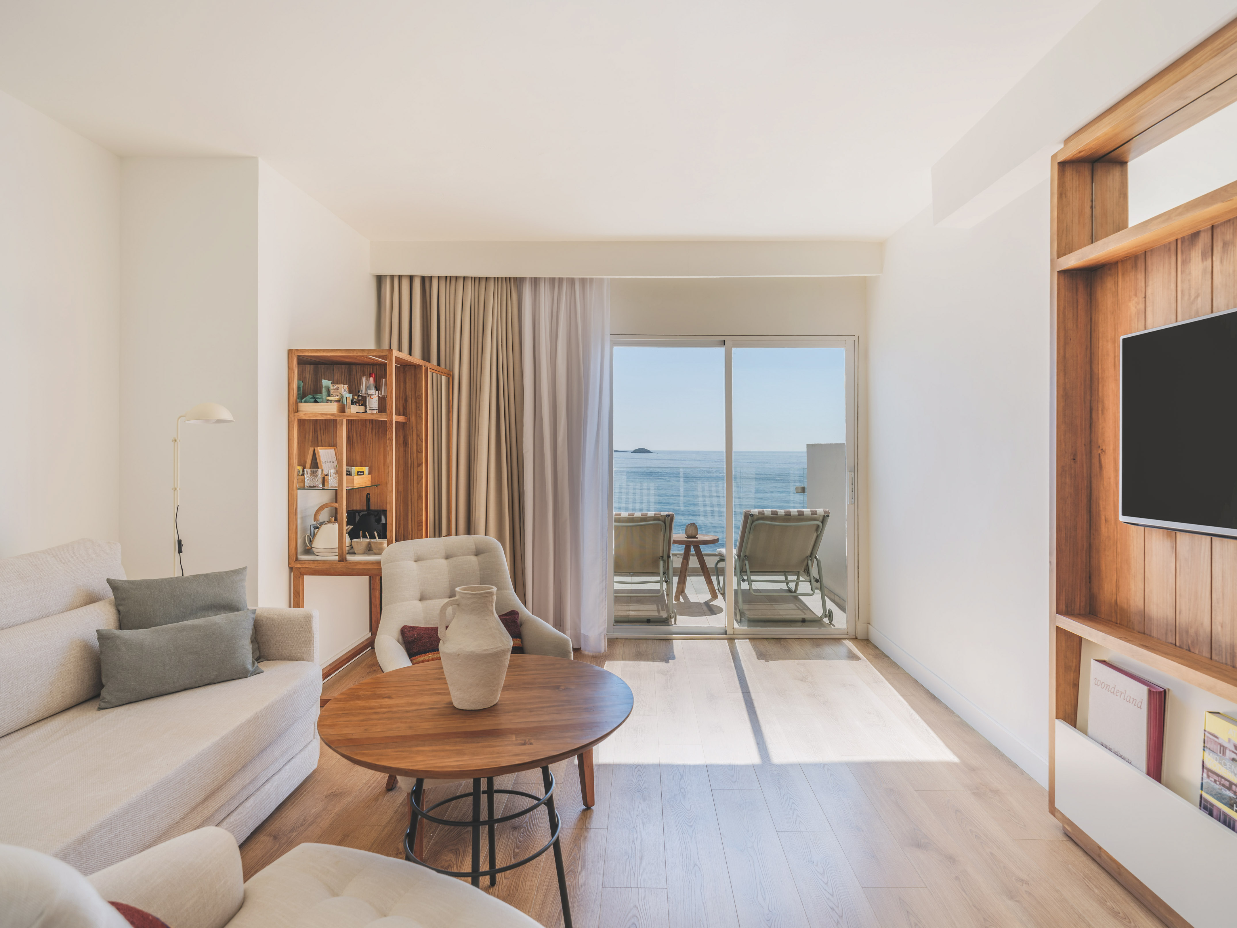 Modern hotel living room with ocean view balcony, light sofa, and wood accents.
