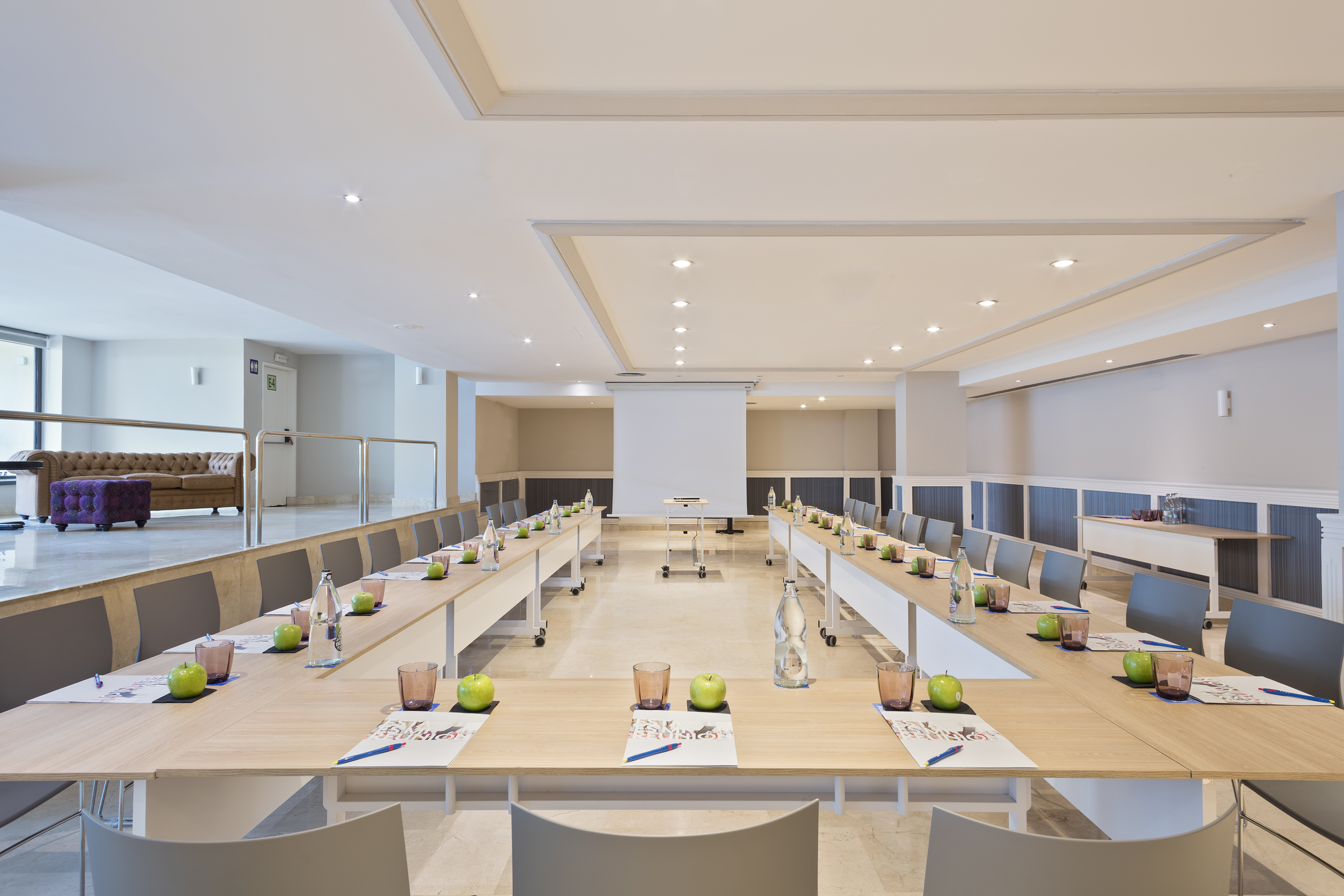 U-shaped modern meeting room setup with projector screen and individual place settings.