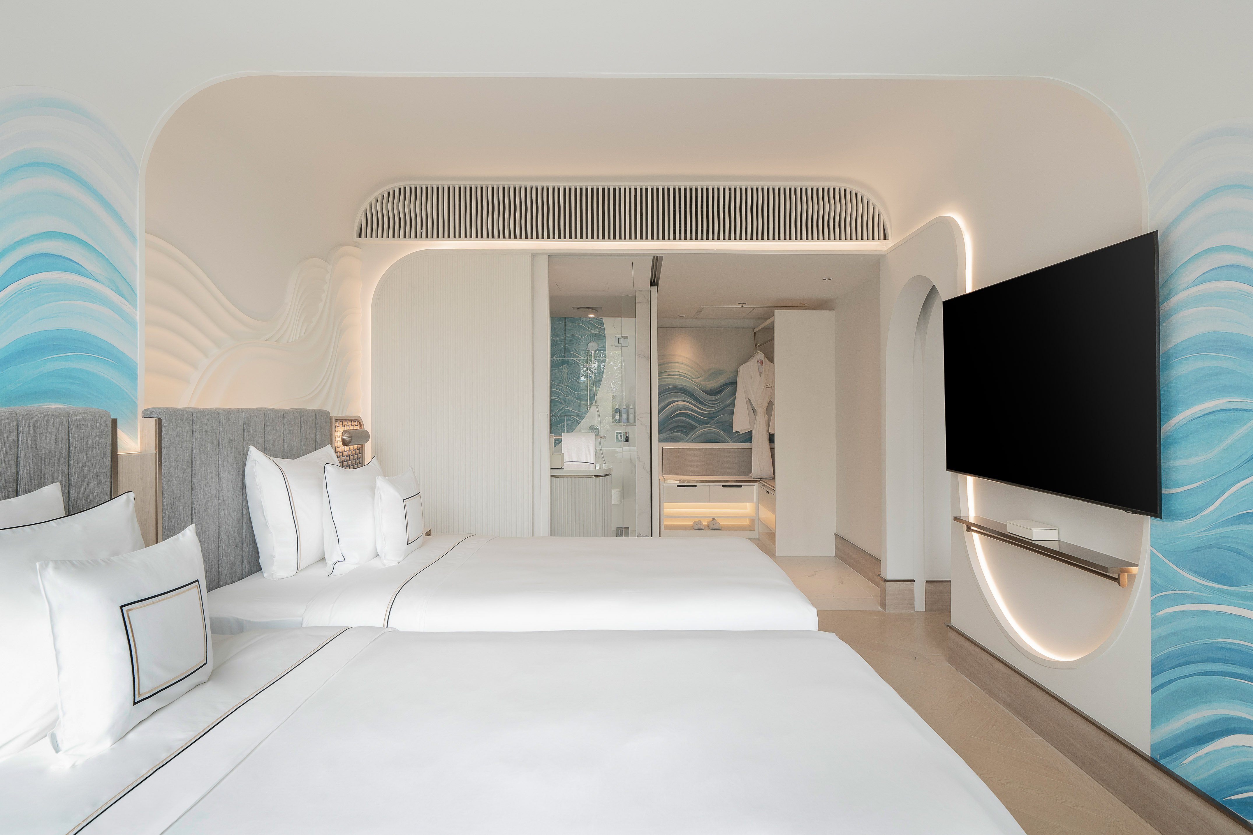 Coastal-themed hotel room with twin beds, blue wave wall art, and TV.