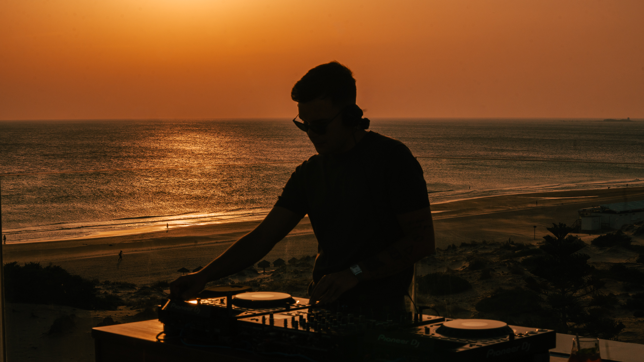 DJ performing a sunset set overlooking a beach and ocean.