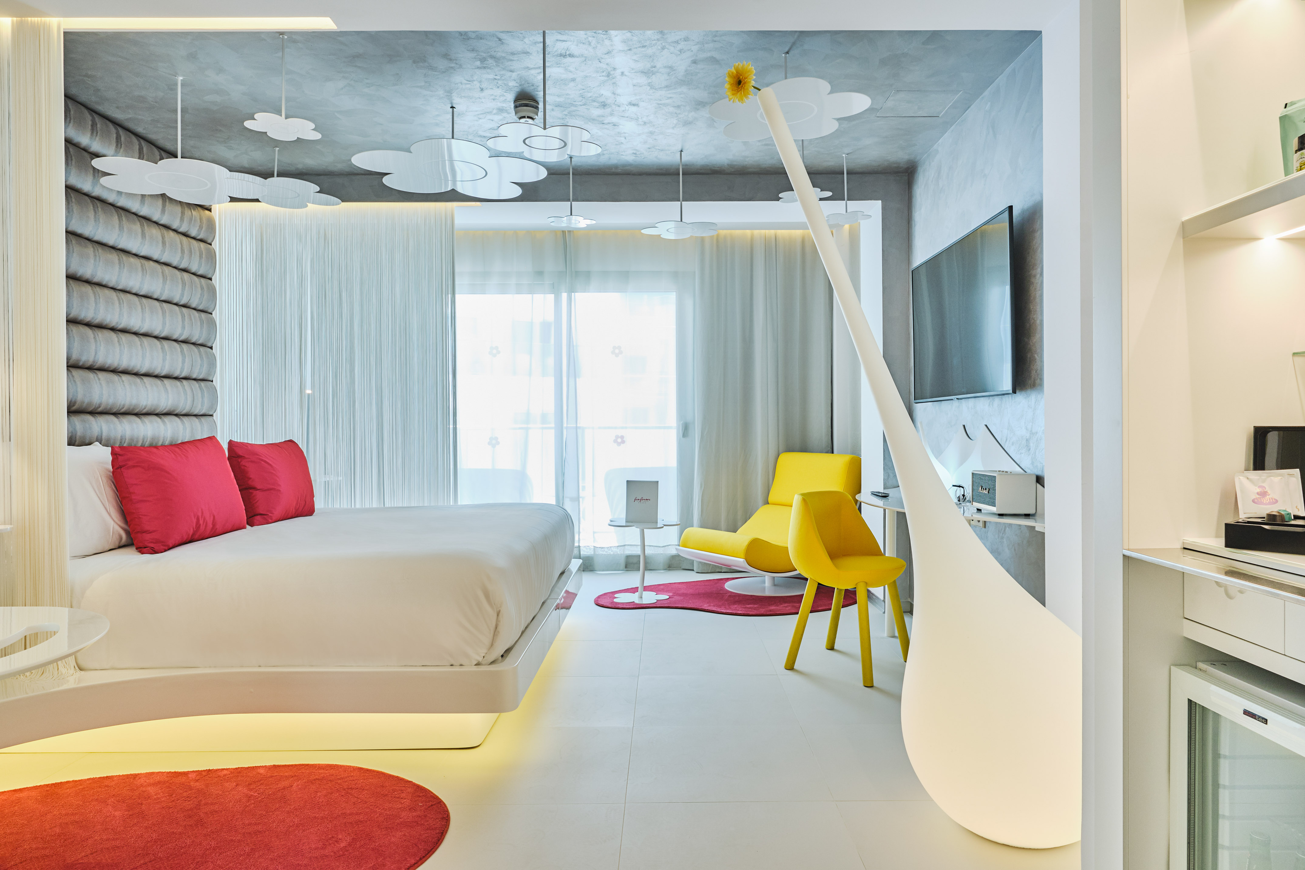 Stylish modern hotel room with floating bed, red accents, yellow furniture, cloud decor.