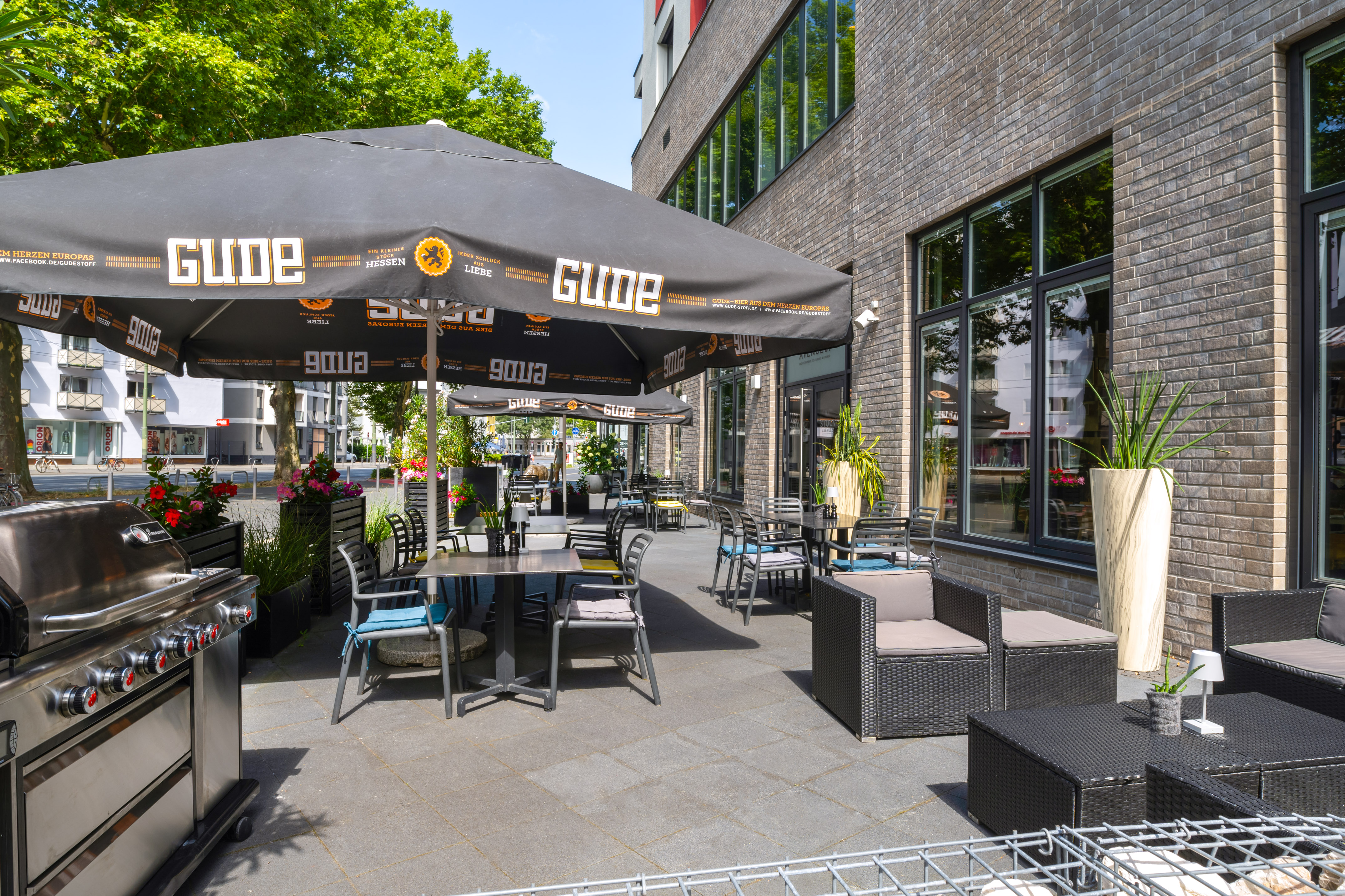 Outdoor cafe patio with Gude umbrellas, seating, and barbecue grill.
