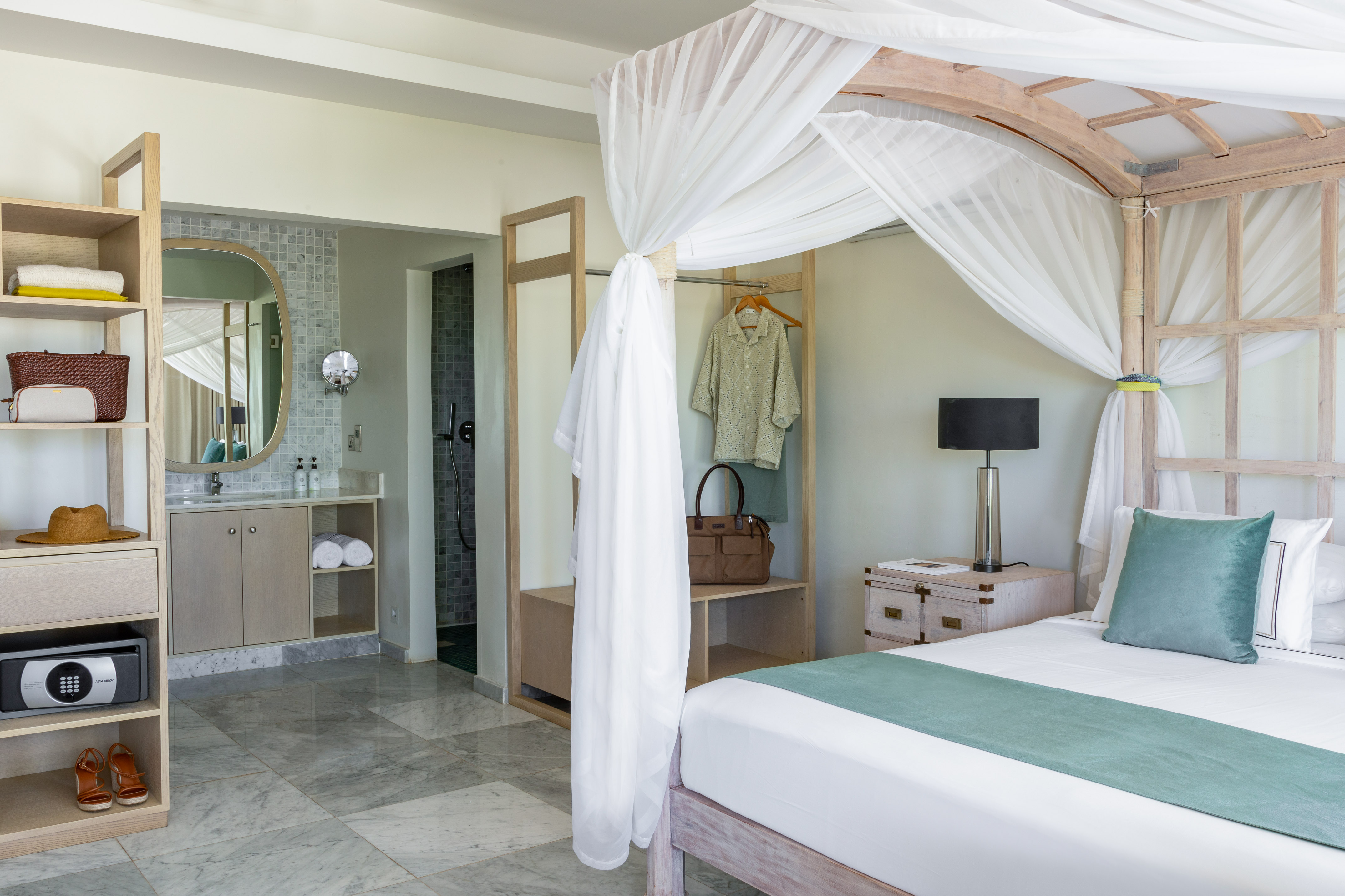 Tropical resort bedroom with canopy bed, ensuite bathroom, and stylish wooden furniture.