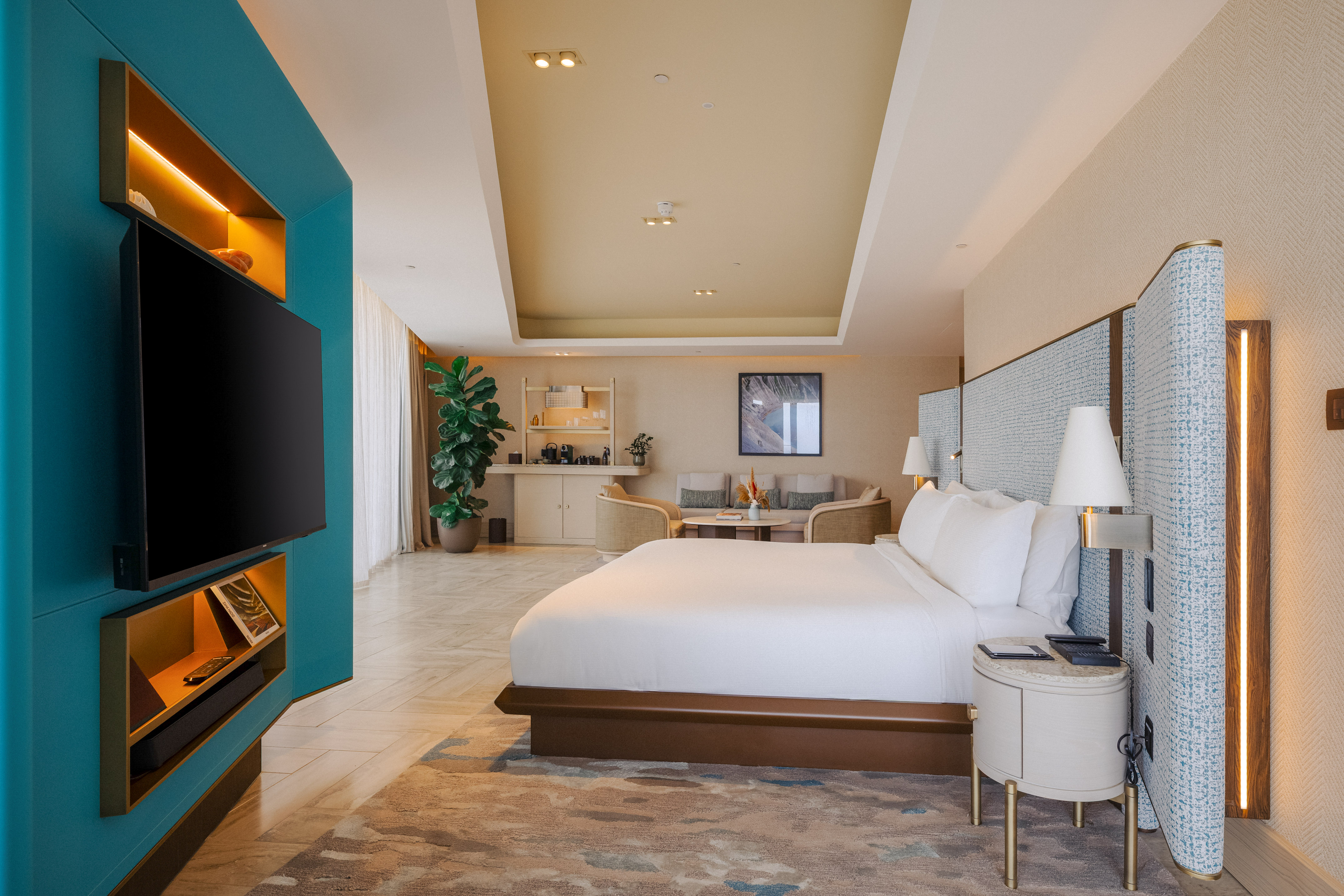 Luxury hotel suite bedroom with modern design, teal wall, king bed, and lounge.