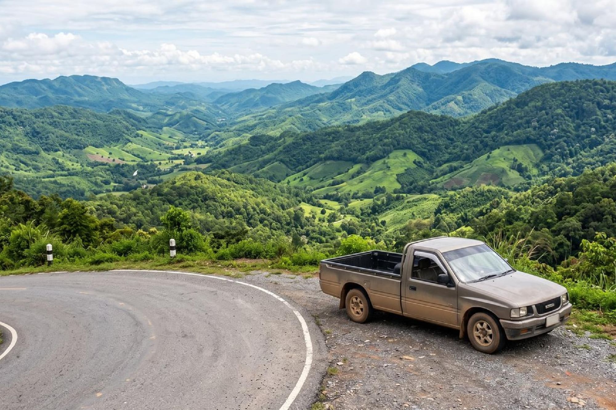 Pickup truck on scenic mountain road overlooking lush green valleys and hills.