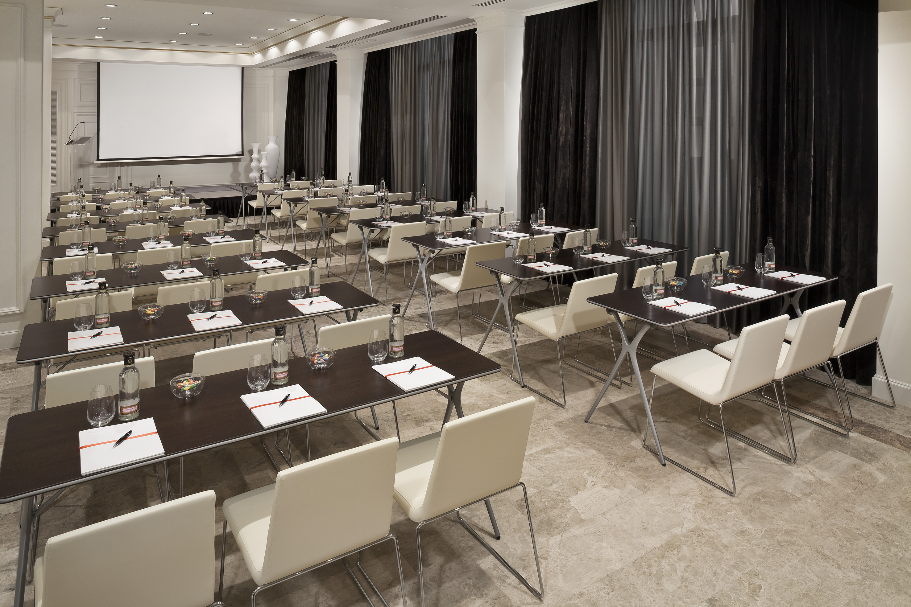 Empty conference room with classroom setup, tables, chairs, and screen.