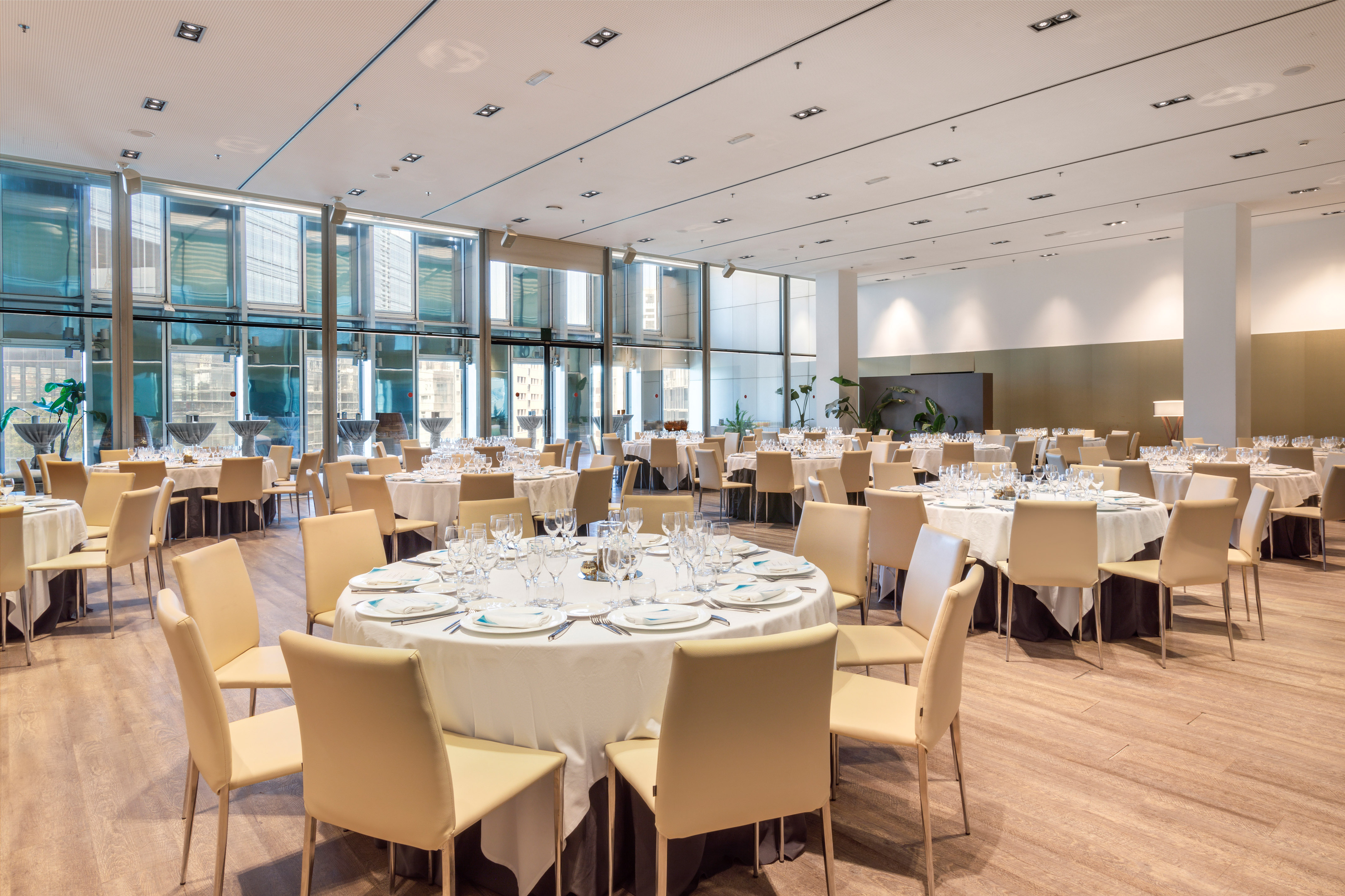 Elegant hotel event space with round tables, chairs, and city window views.