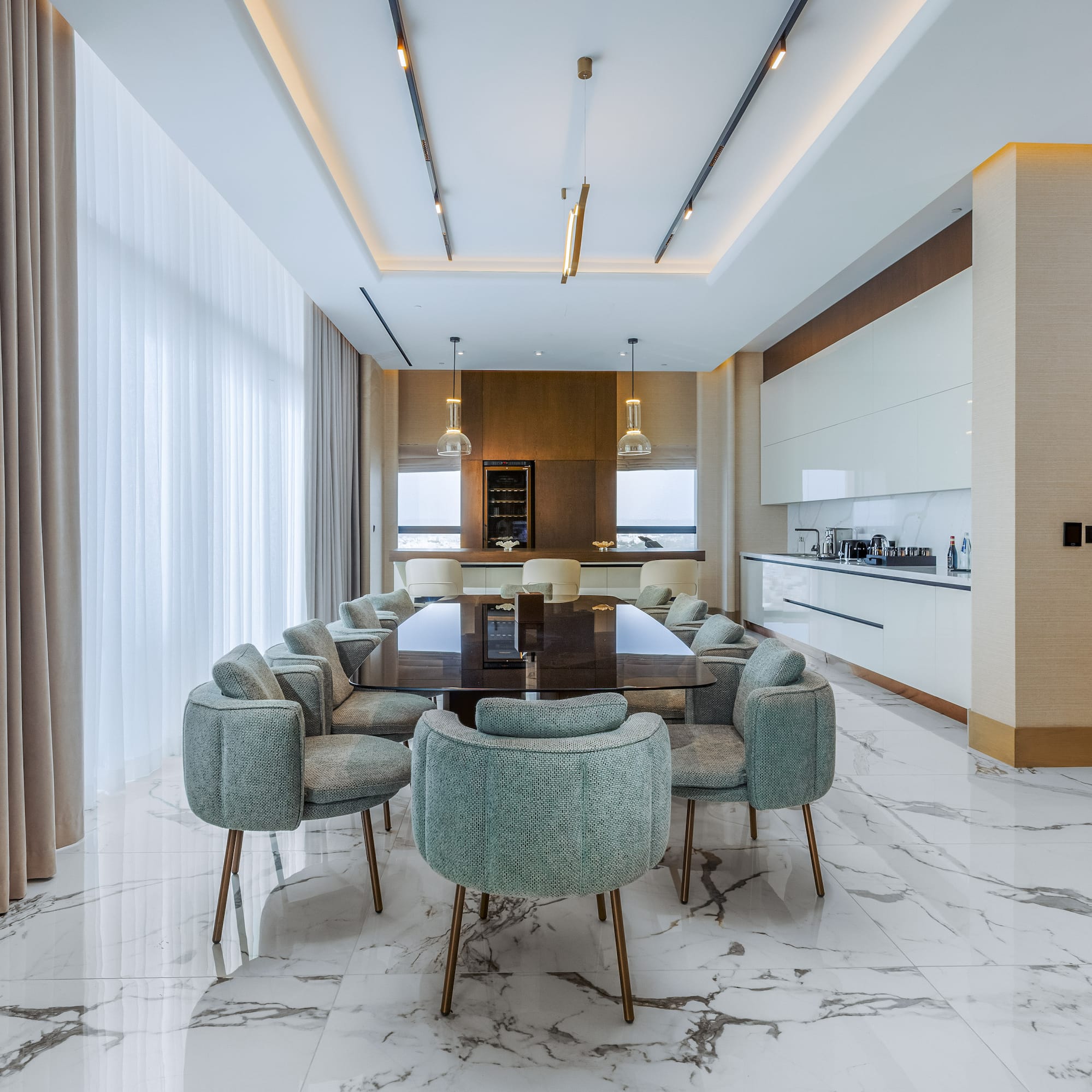 Modern luxury dining room with marble floor, large table, green chairs, and integrated kitchen.