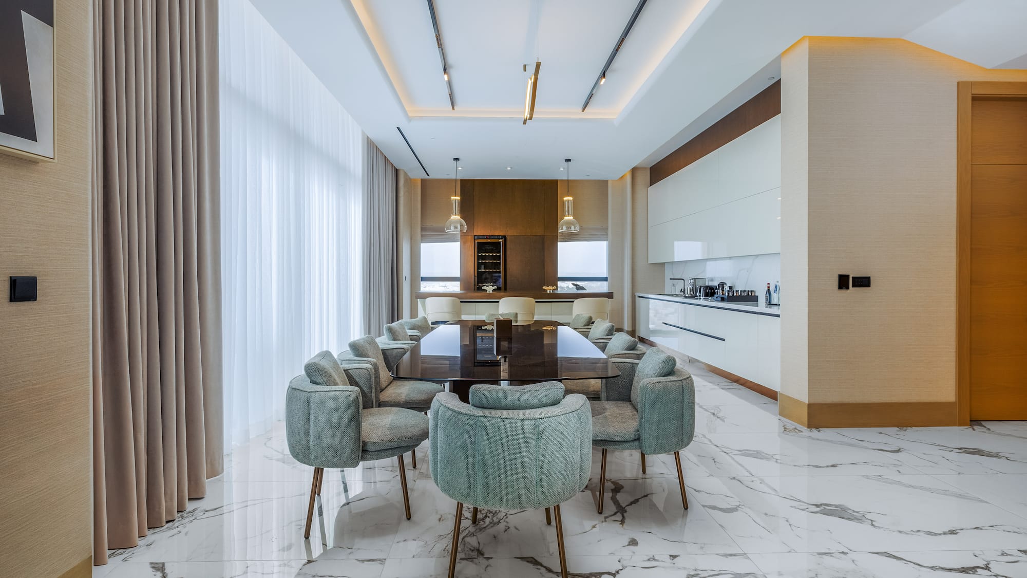 Modern luxury dining room with marble floor, large table, green chairs, and integrated kitchen.