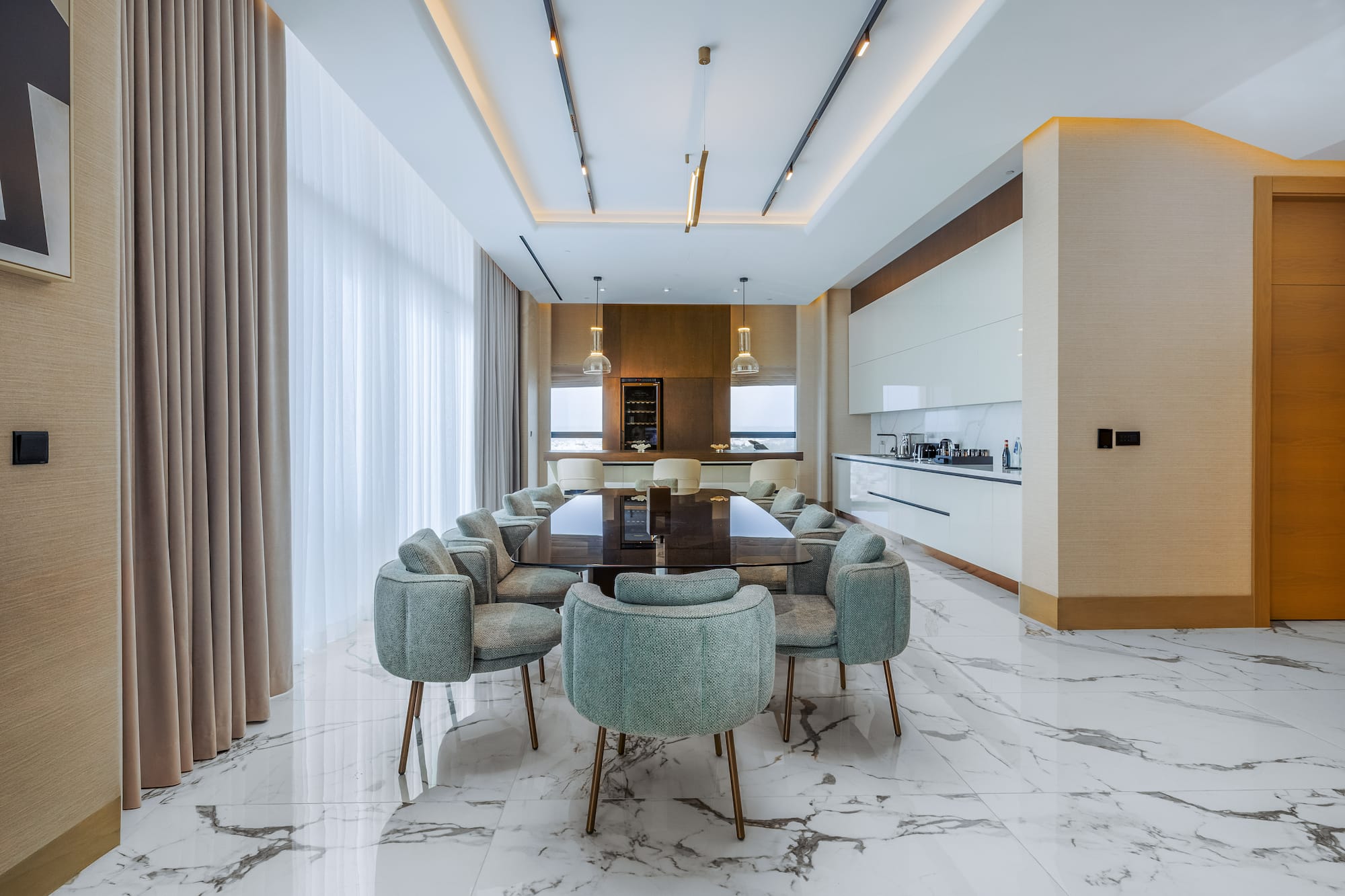 Modern luxury dining room with marble floor, large table, green chairs, and integrated kitchen.