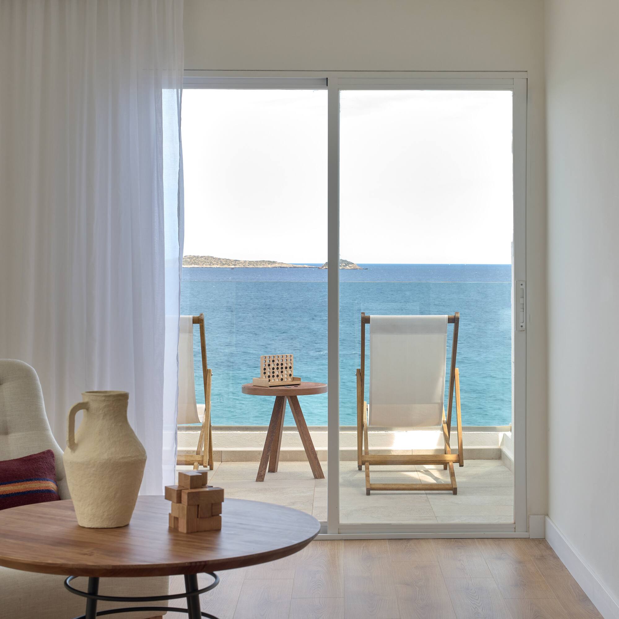 Modern hotel room with sea view balcony, lounge chairs, and blue ocean.