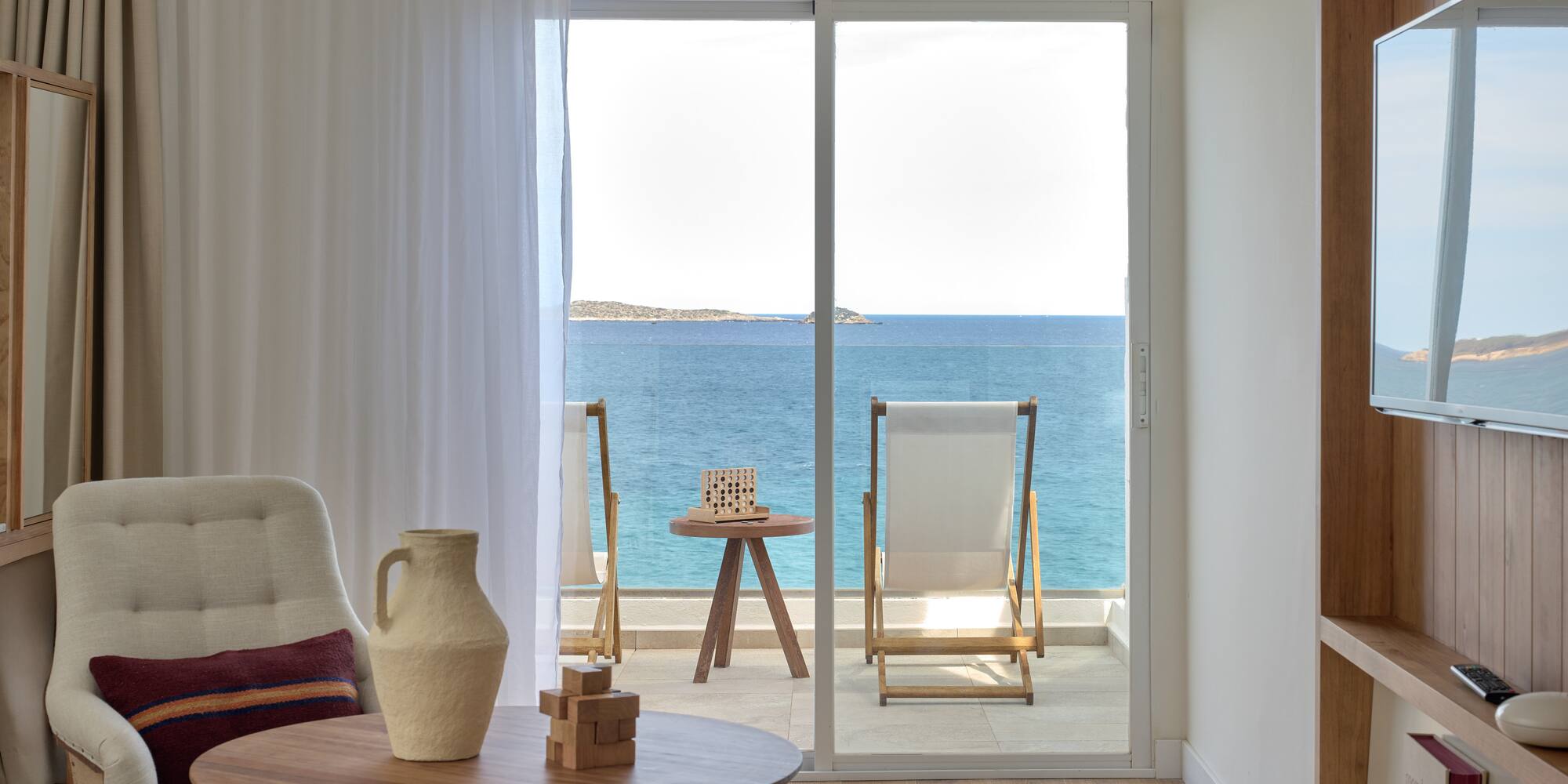 Modern hotel room with sea view balcony, lounge chairs, and blue ocean.