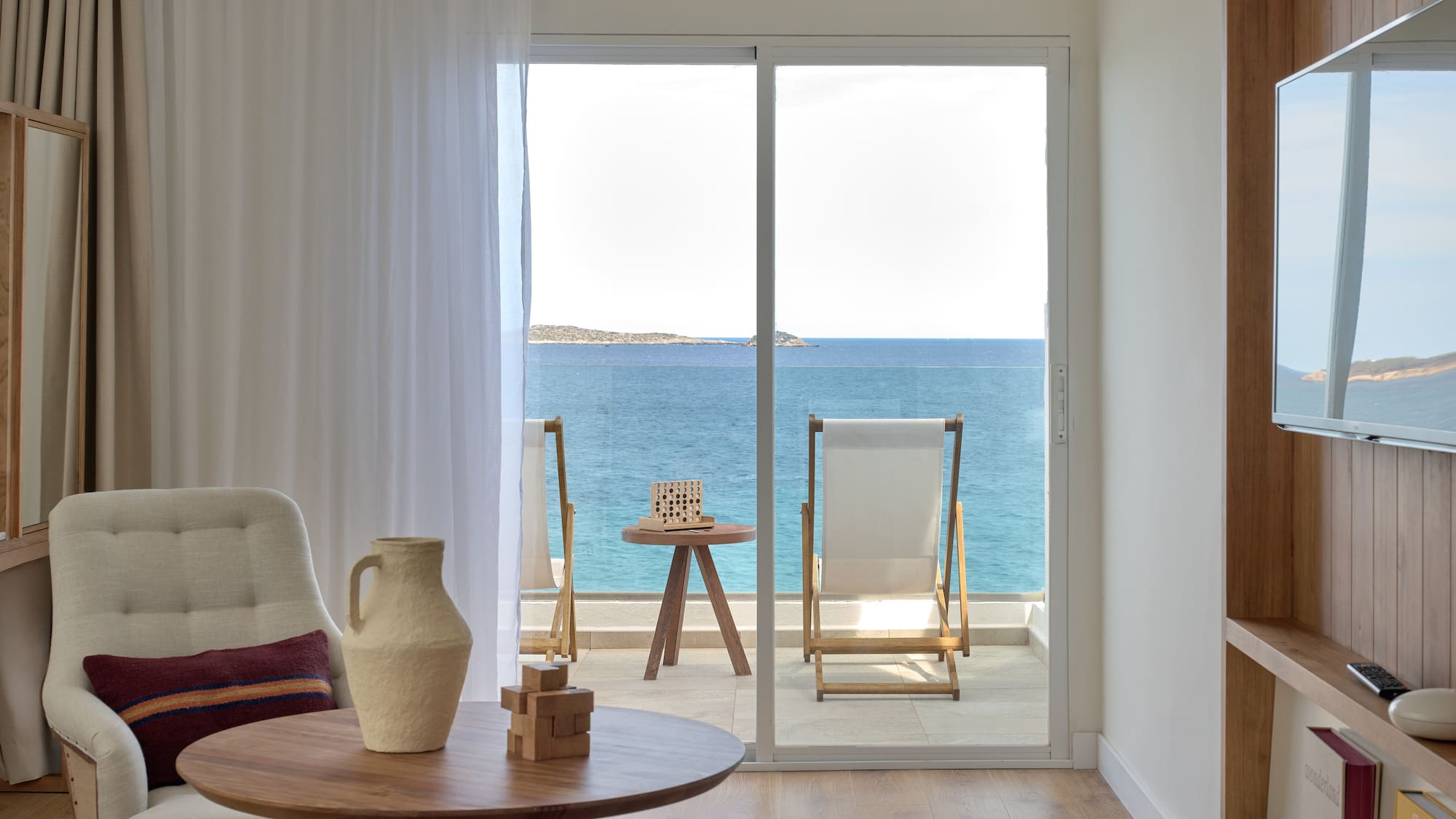 Modern hotel room with sea view balcony, lounge chairs, and blue ocean.