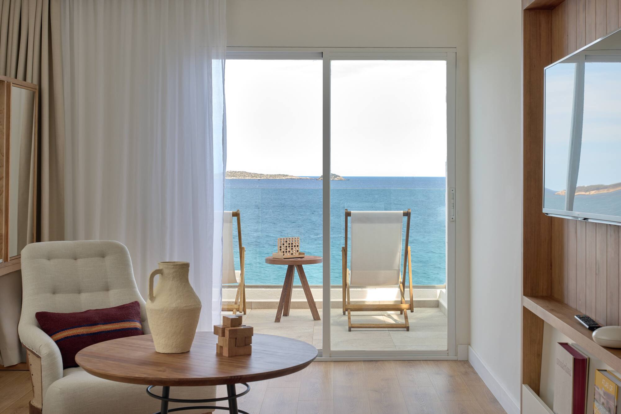 Modern hotel room with sea view balcony, lounge chairs, and blue ocean.