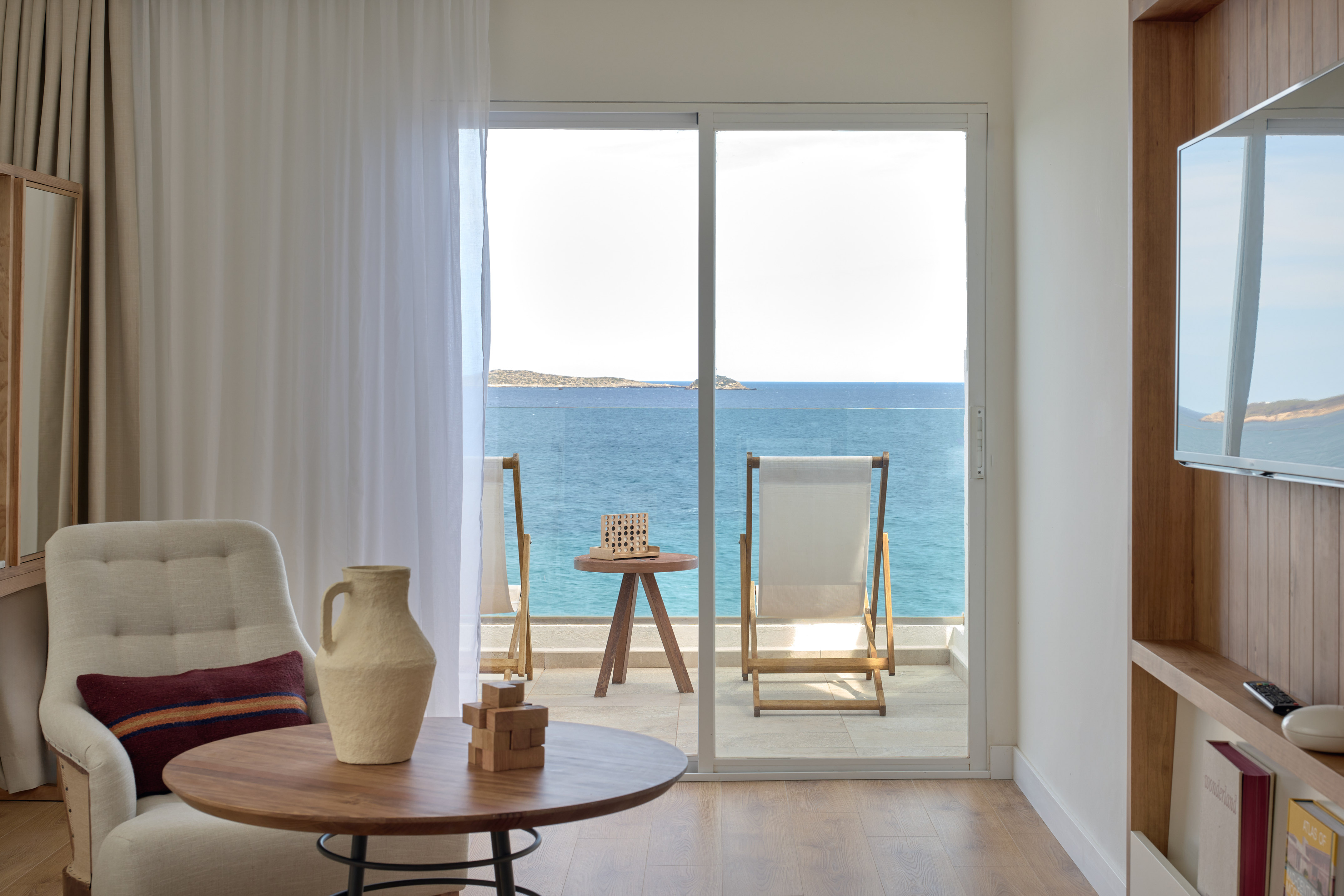 Modern hotel room with sea view balcony, lounge chairs, and blue ocean.