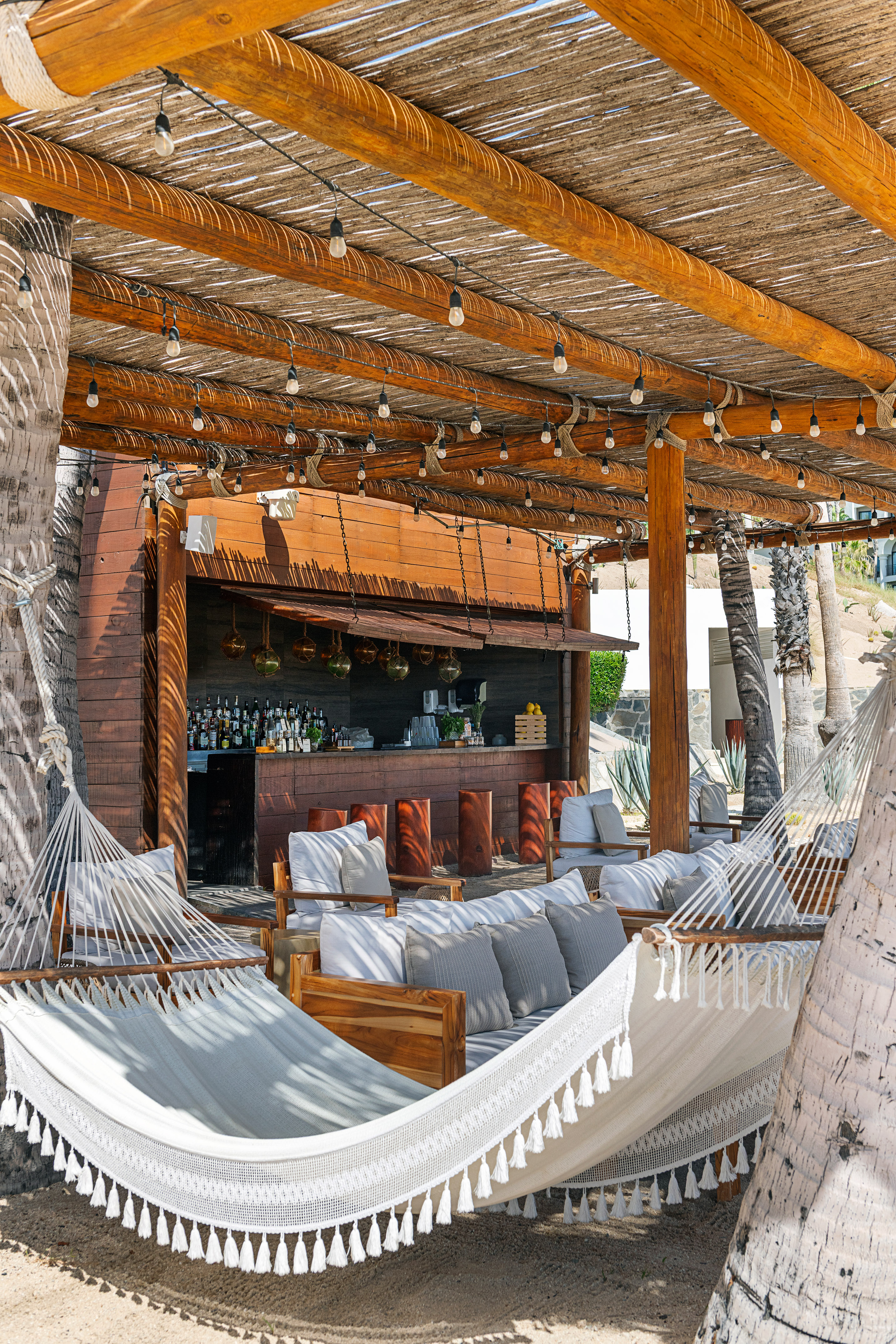 Tropical resort bar with hammocks, lounge seating, and thatched roof.