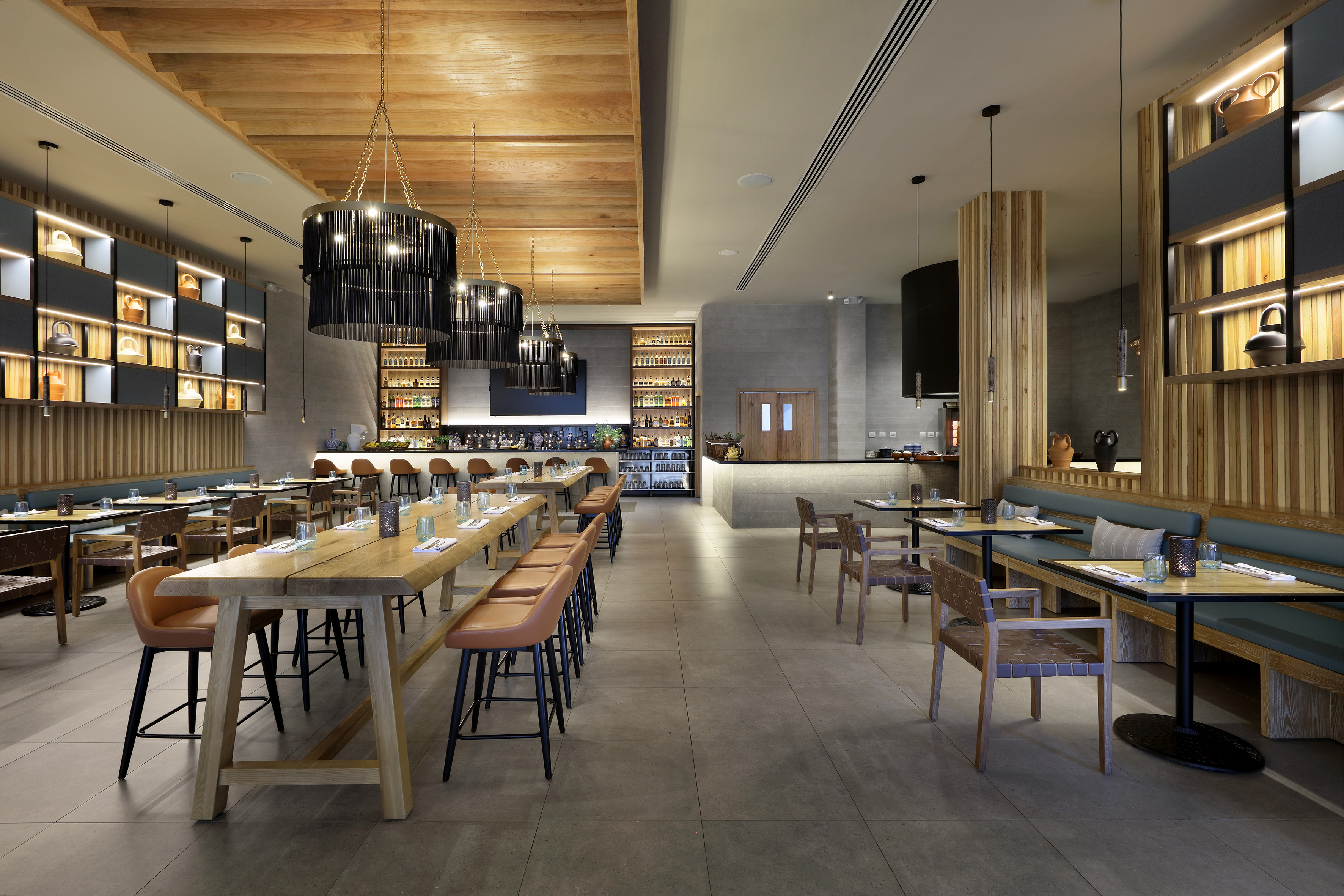 Modern restaurant dining room and bar with long wooden tables and stylish lighting.
