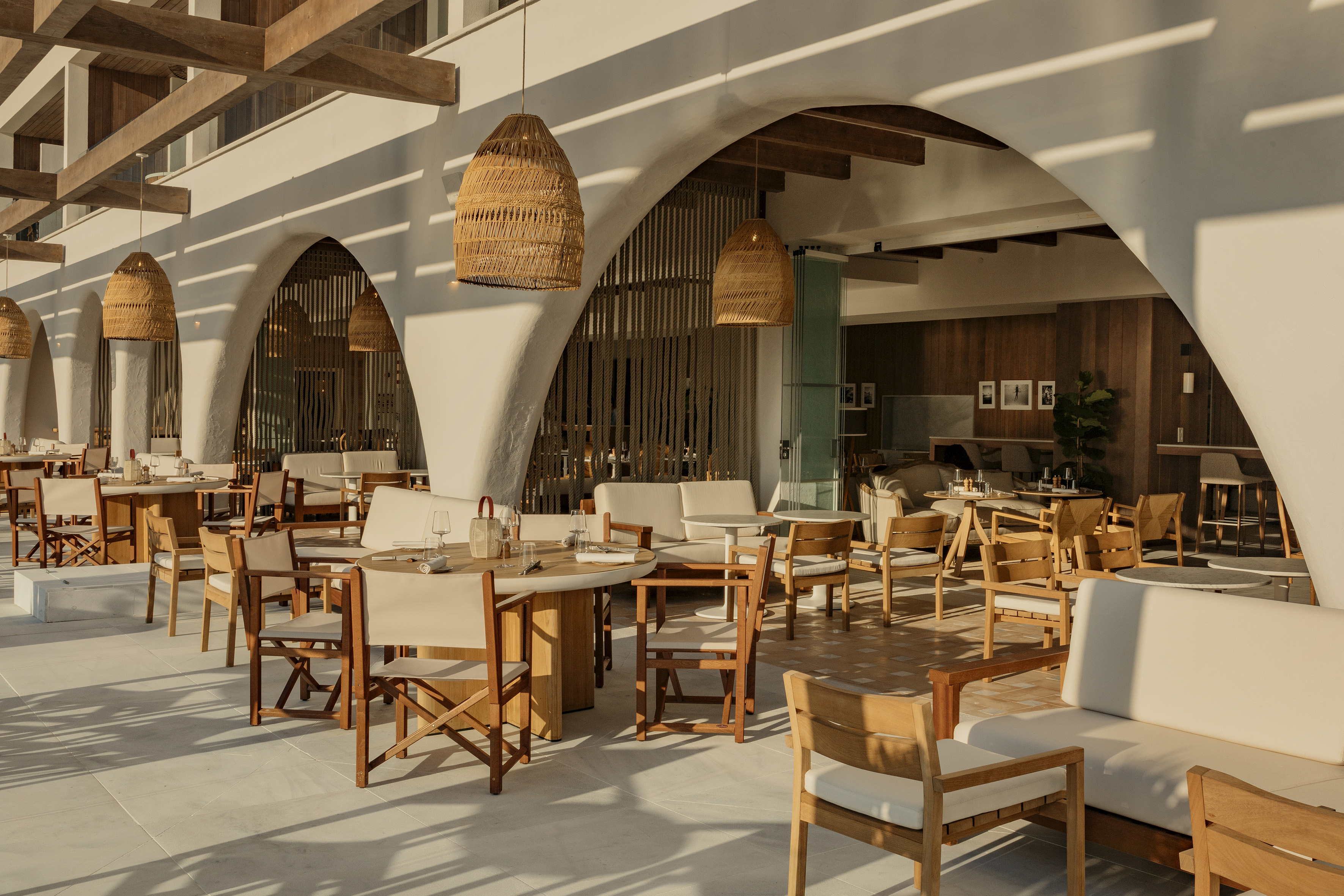 Resort restaurant with arched walls, natural wood seating, and wicker pendant lights.