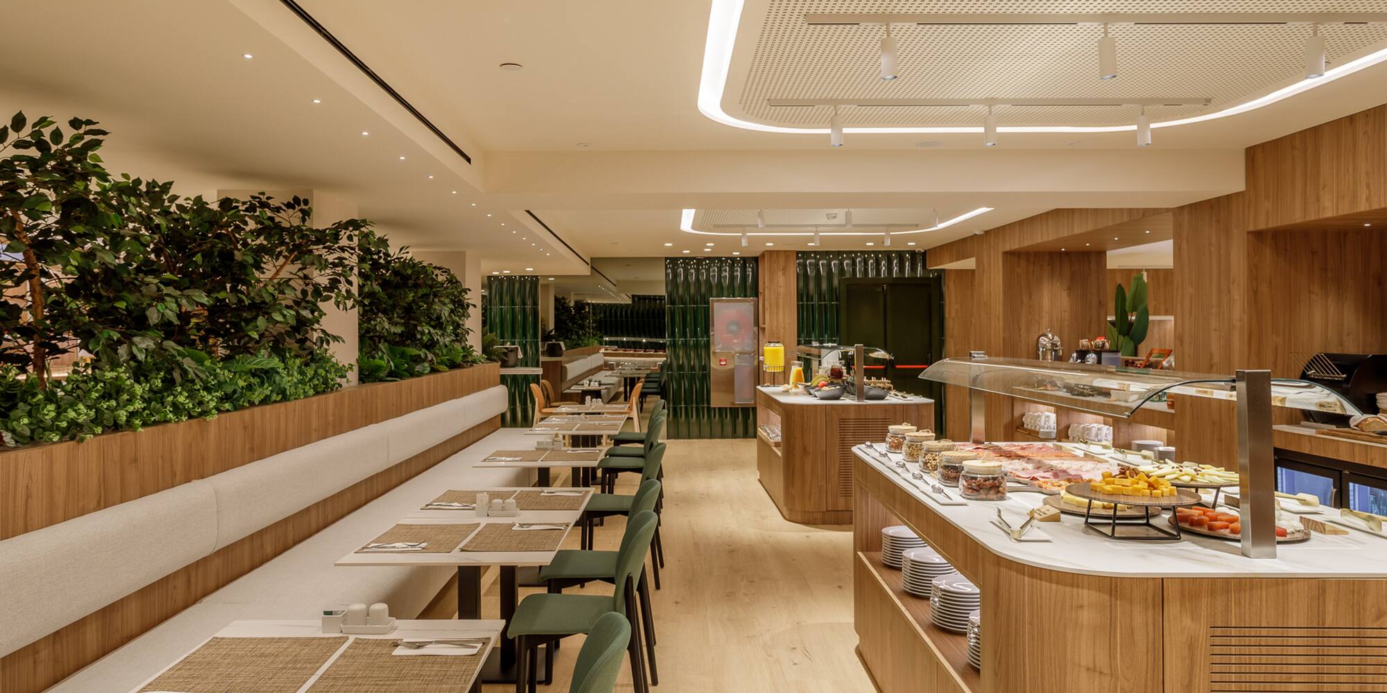 Modern hotel breakfast buffet, wood interior, green plants, and dining tables.