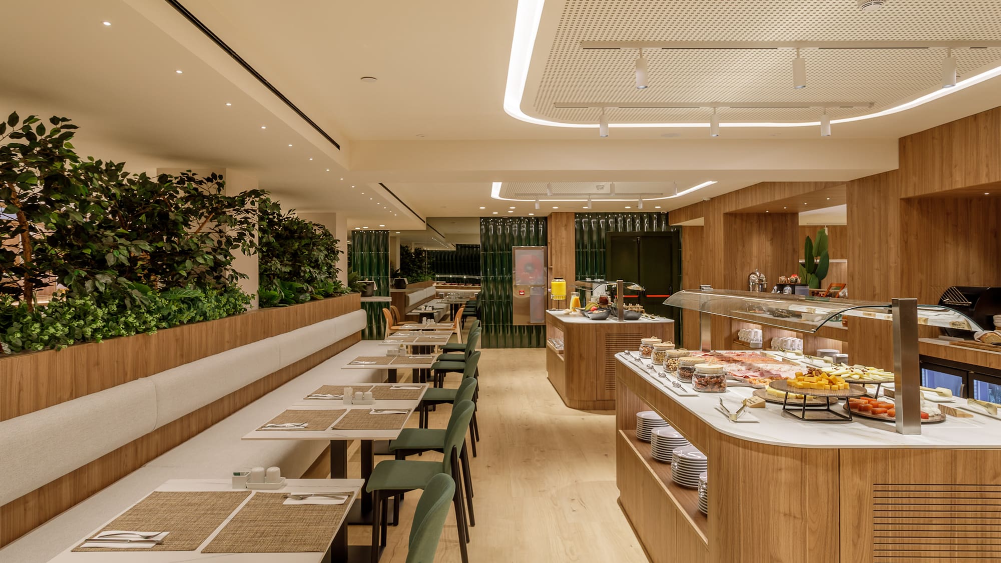 Modern hotel breakfast buffet, wood interior, green plants, and dining tables.