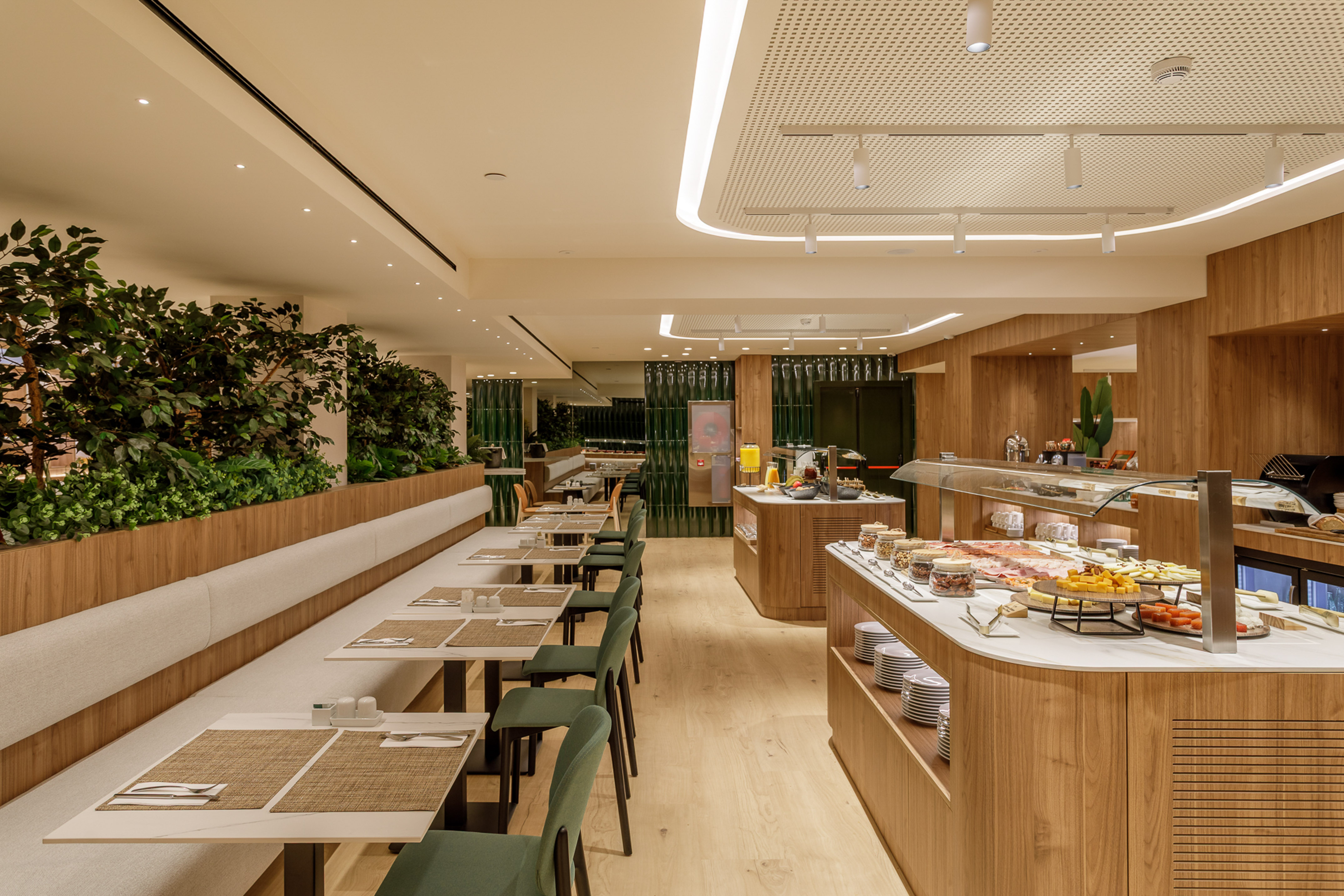 Modern hotel breakfast buffet, wood interior, green plants, and dining tables.