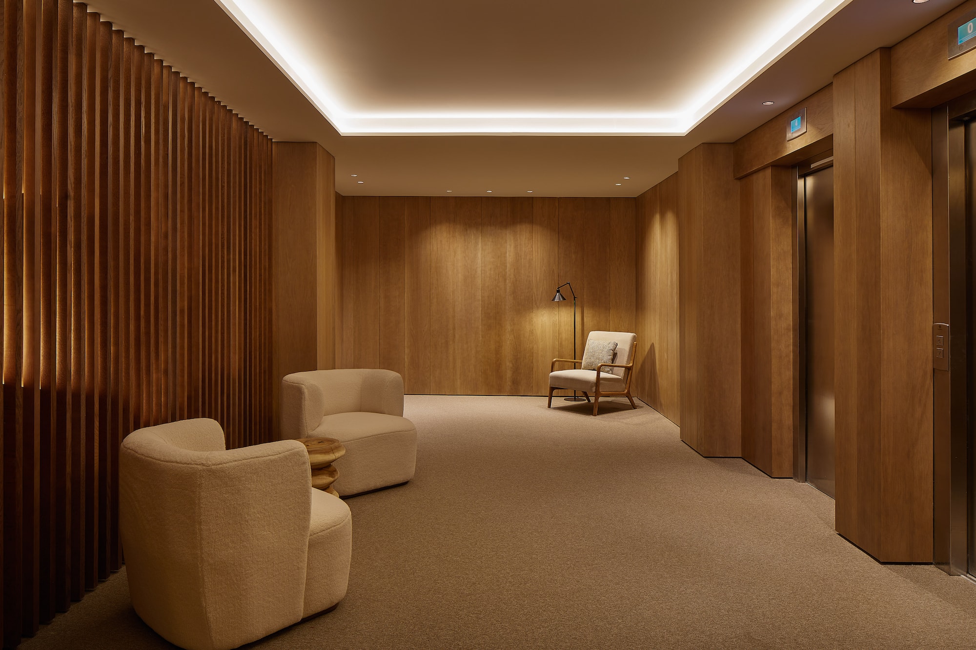 Modern wooden lobby with lounge chairs, warm lighting, and elevator entrance.