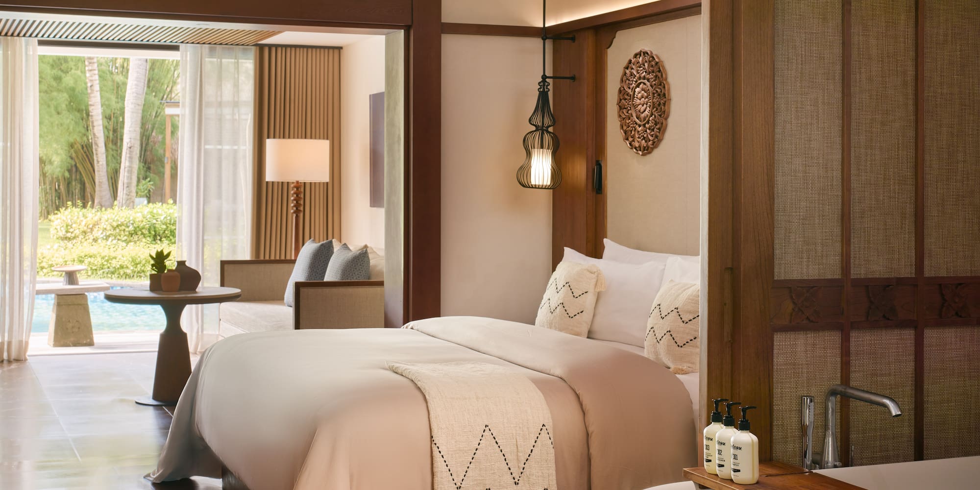Luxury hotel suite with bed, freestanding bathtub, and lush pool garden view.