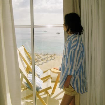 a woman standing in front of a window looking out to the ocean