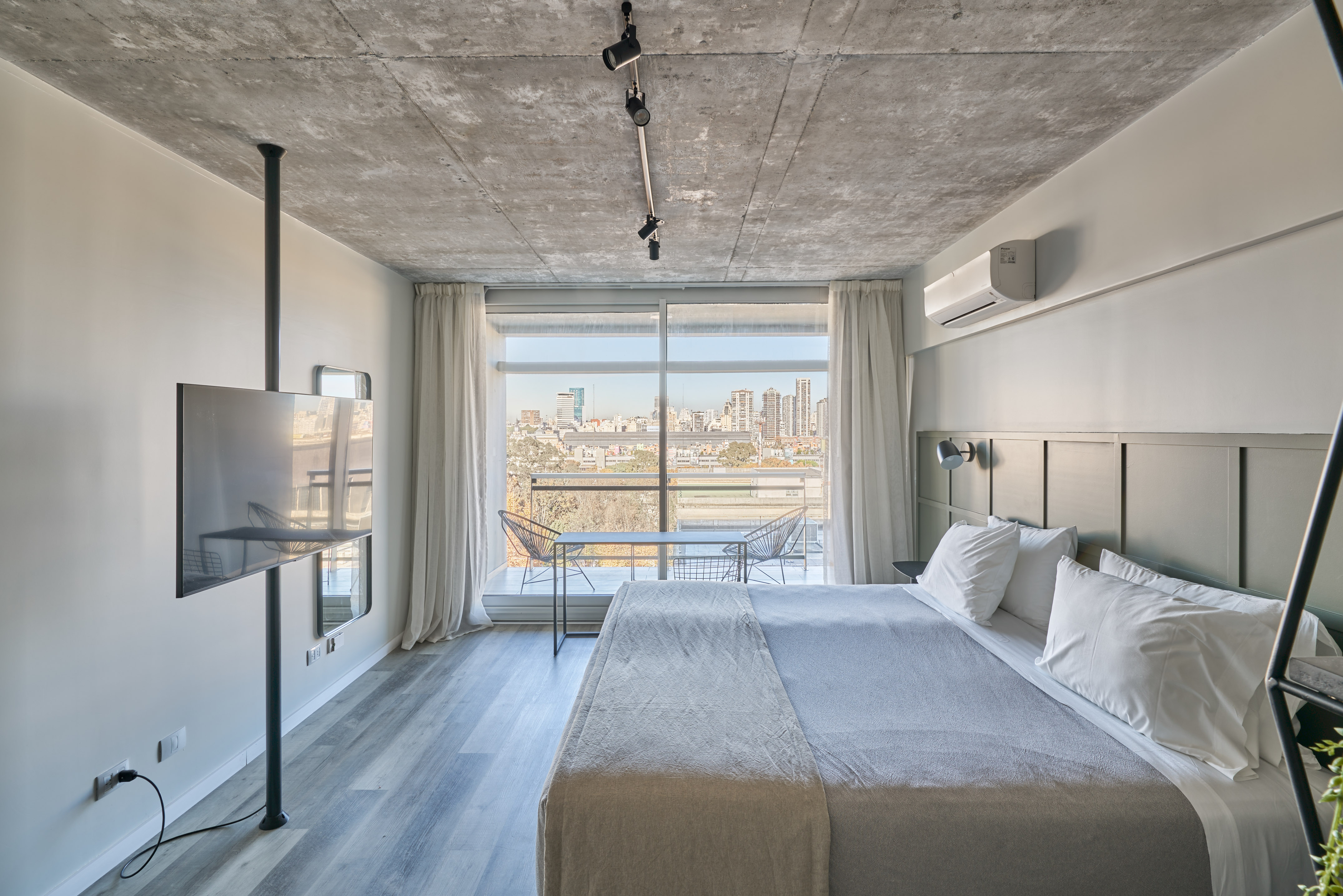 Modern bedroom with city view balcony, concrete ceiling, and king bed.