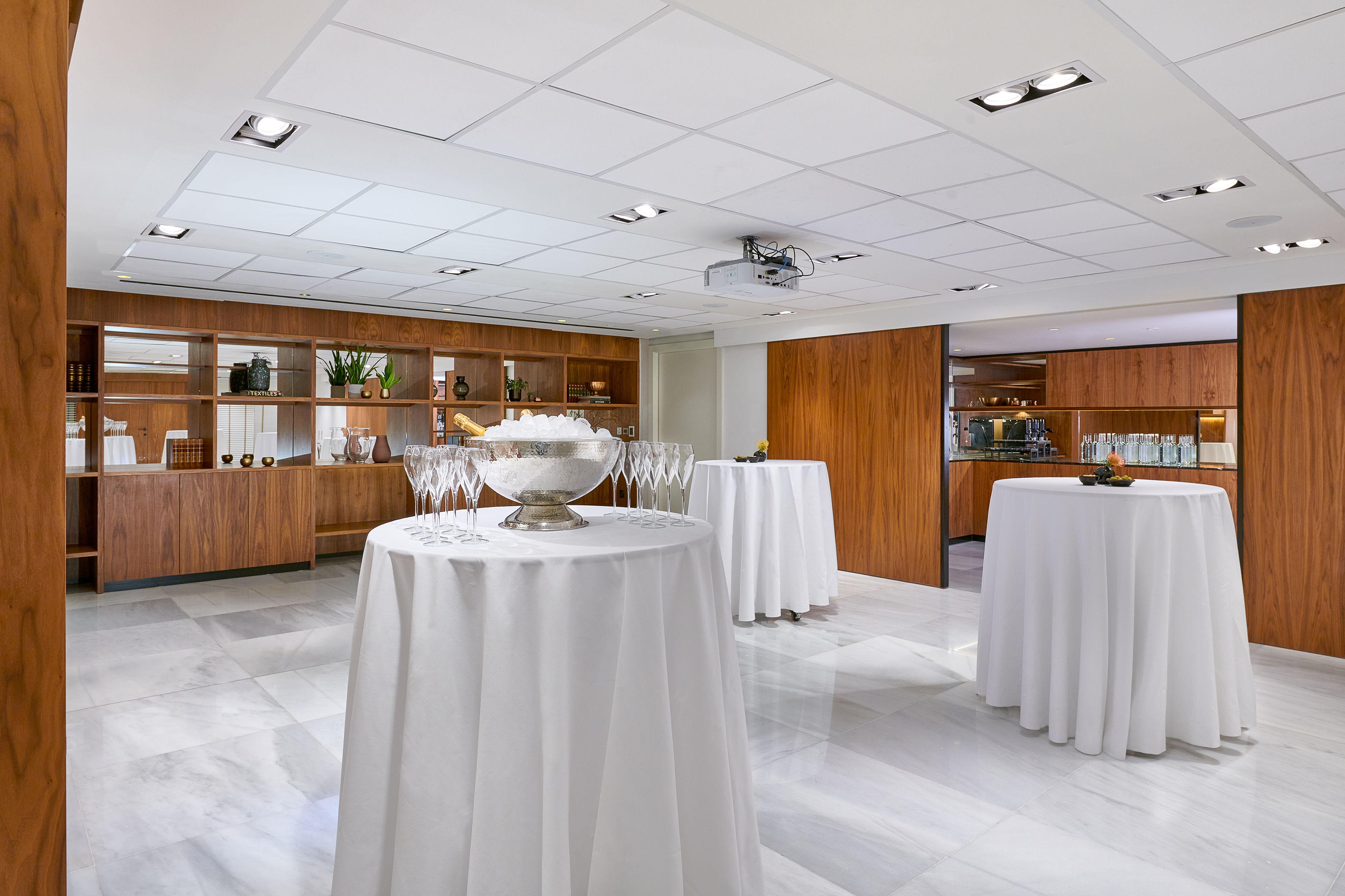 Elegant event space with white cocktail tables, champagne, and wood decor.