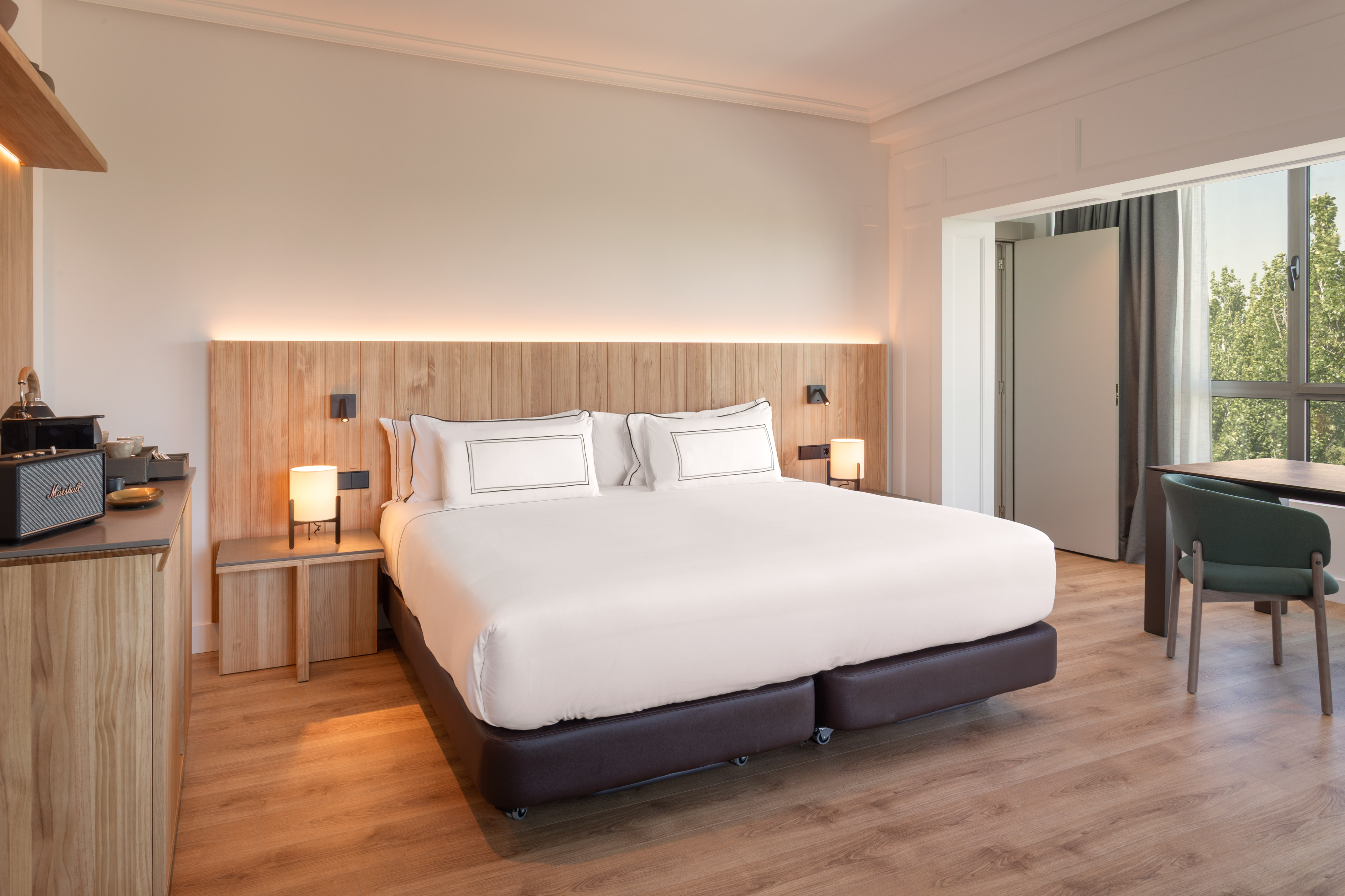 Modern hotel room with king bed, wooden headboard, natural light, and workspace.