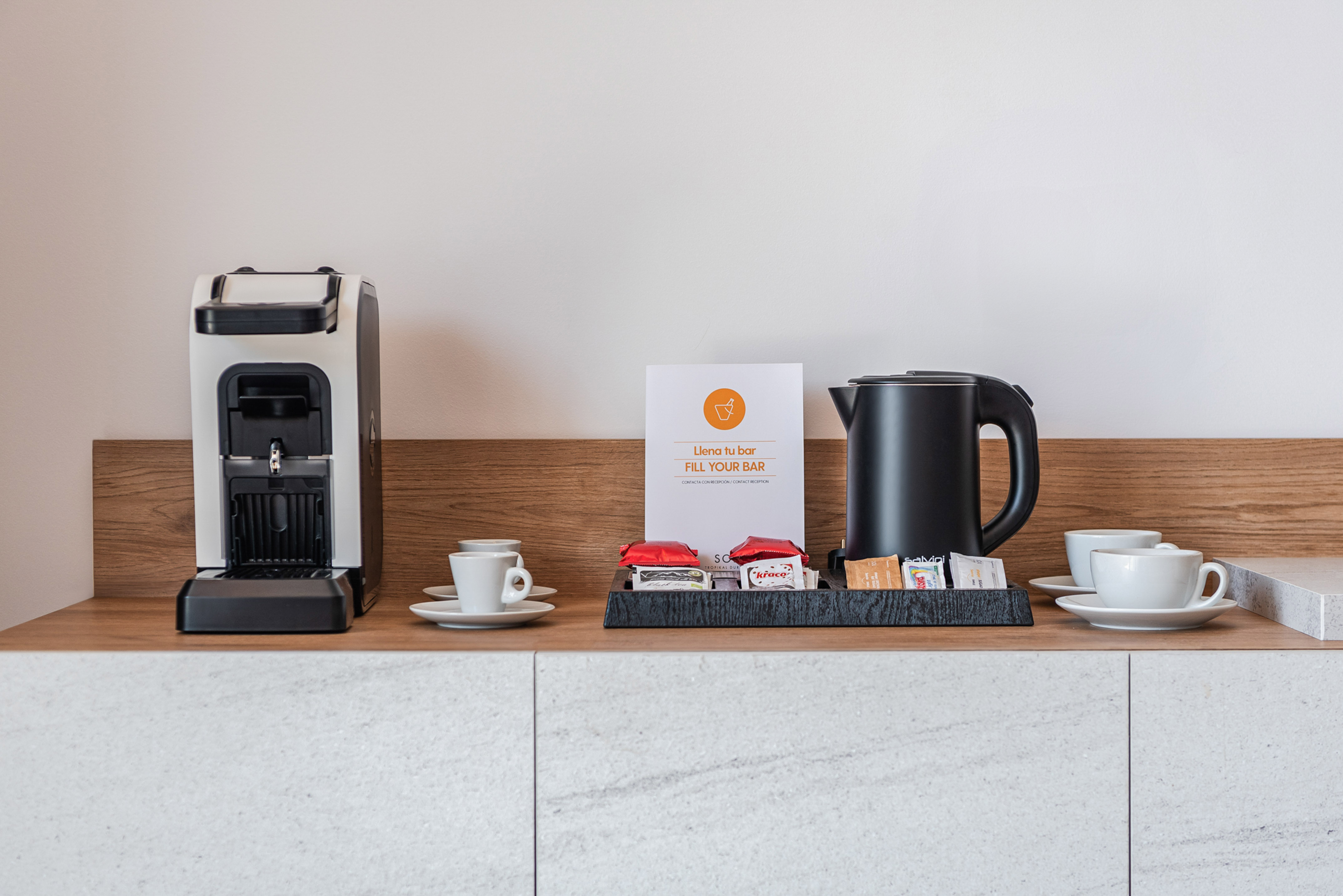 Hotel room coffee station: espresso machine, kettle, cups, and snacks.