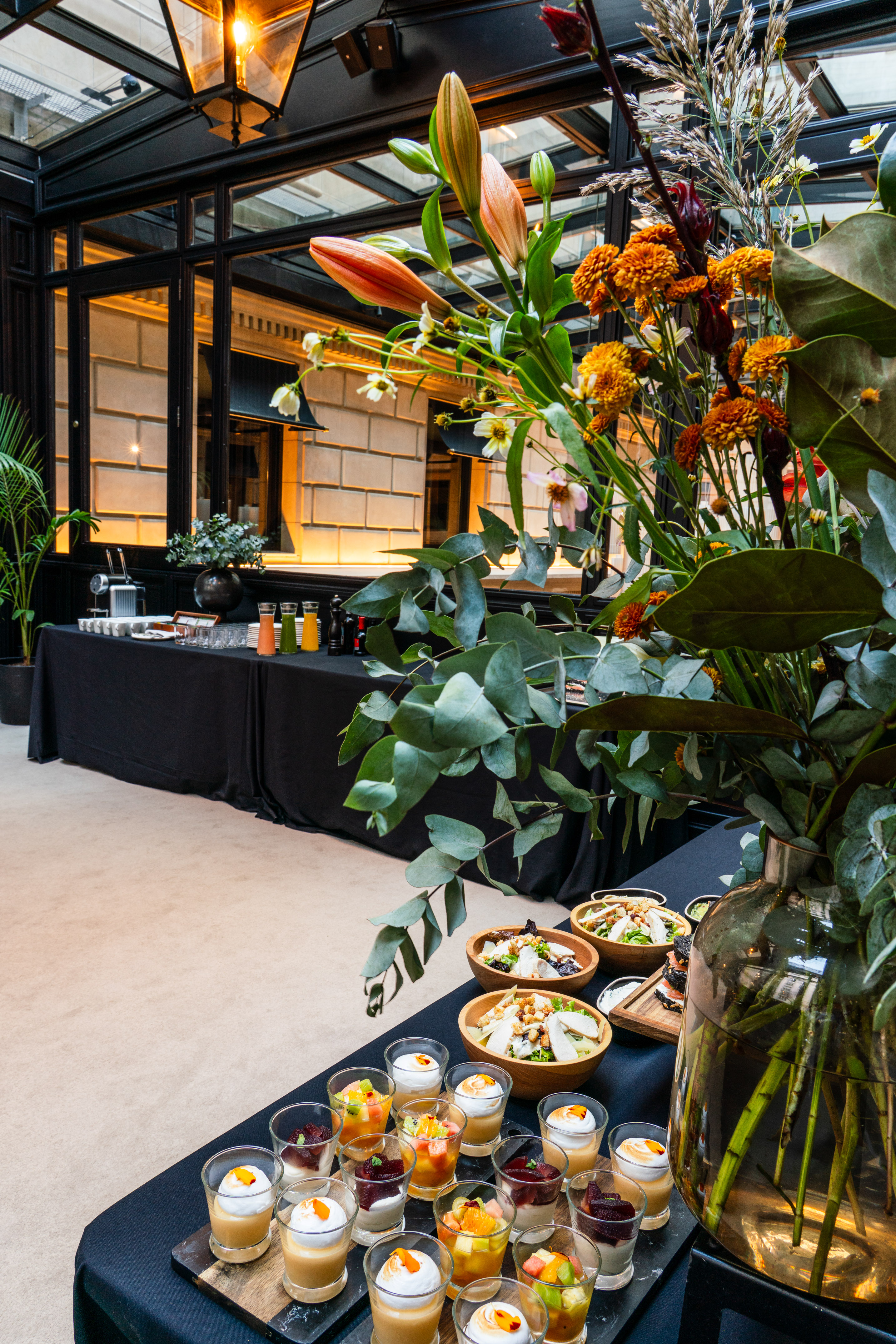 Indoor buffet with salads, desserts, juices, and orange flower arrangement.