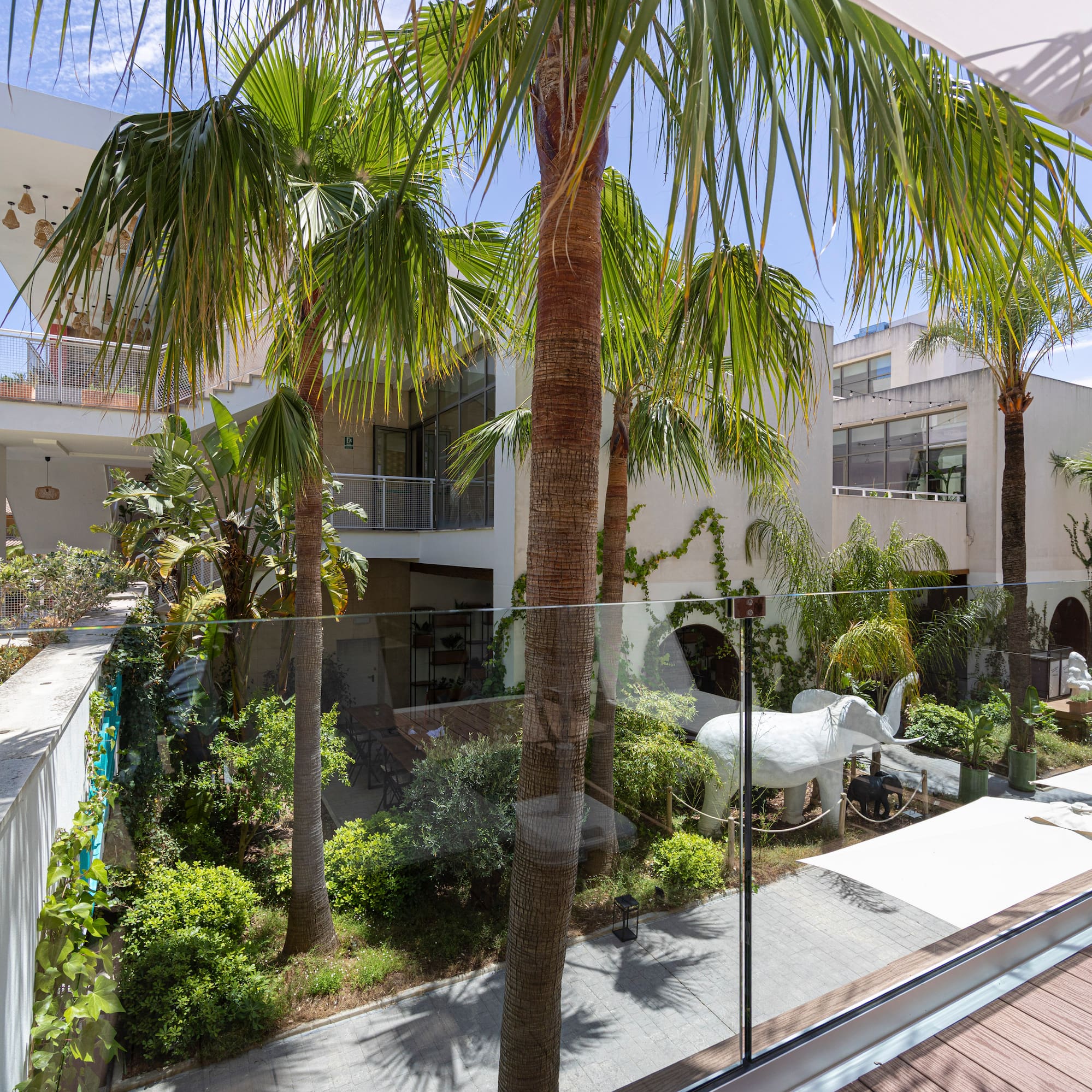 Balcony view: Modern tropical hotel courtyard with palm trees and white elephant.